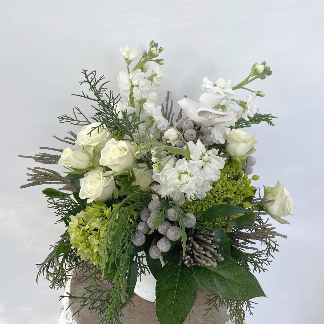 Dove of Peace - A Touch of Serenity for the Season Embrace the beauty of simplicity with our Dove of Peace arrangement, a graceful blend of clean whites and crisp greens. Perfect for expressing hope, peace, or thoughtful holiday wishes. -Elegant Blooms: Features hydrangeas, tiny roses, stock, and berry clusters for a soft, serene look. -Timeless Design: A simple yet sophisticated arrangement that embodies the season's spirit. -Meaningful Gesture: Adorned with a symbolic dove, it is ideal for gifting or as a calming centerpiece in your home. Share a heartfelt message of peace and hope with the Dove of Peace, a timeless reminder of the season’s true meaning.