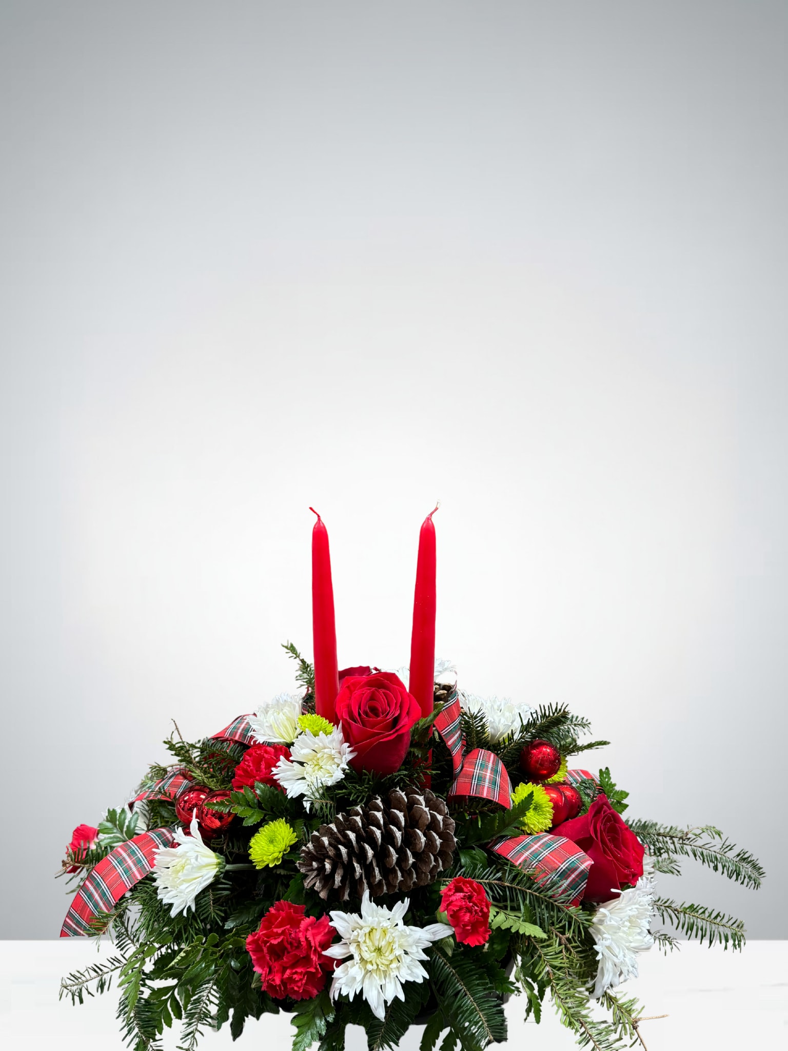Holiday Magic Centerpiece  - Bring the warmth of Christmas to your table with our Thankful Blessings Centerpiece. Bursting with rich Christmas colors, this festive arrangement features a delightful mix of blooms and greenery, accented with a decorative bow and glowing taper candles. It’s the perfect finishing touch for your Christmas table.