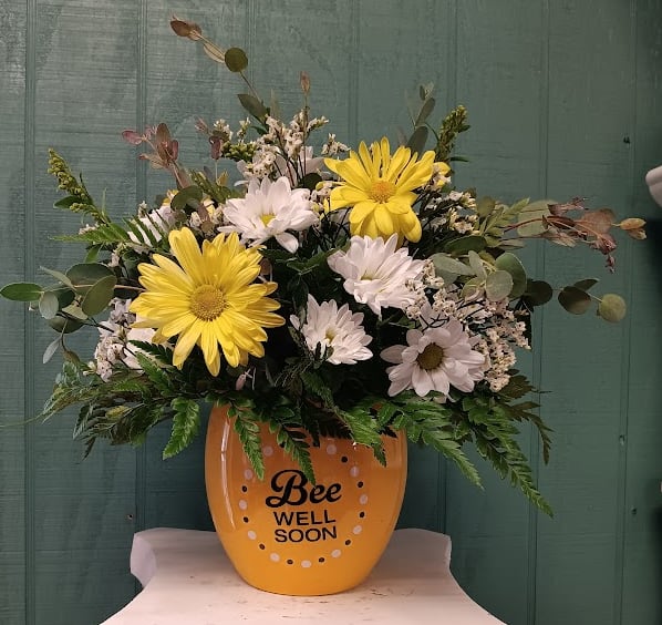 Bee Well - Send a little sunshine with our charming "Bee Well" arrangement!  Featuring cheerful white and yellow daisies, lush greenery, and delicate filler blooms in a classic ceramic dish, this sweet display is perfect for brightening a hospital room or lifting the spirits of someone on the mend. Like a warm hug in flower form, it’s a beautiful way to say “feel better soon!”  Upgrading to Deluxe or Premium will include elegant yellow or white roses for an extra-special touch.