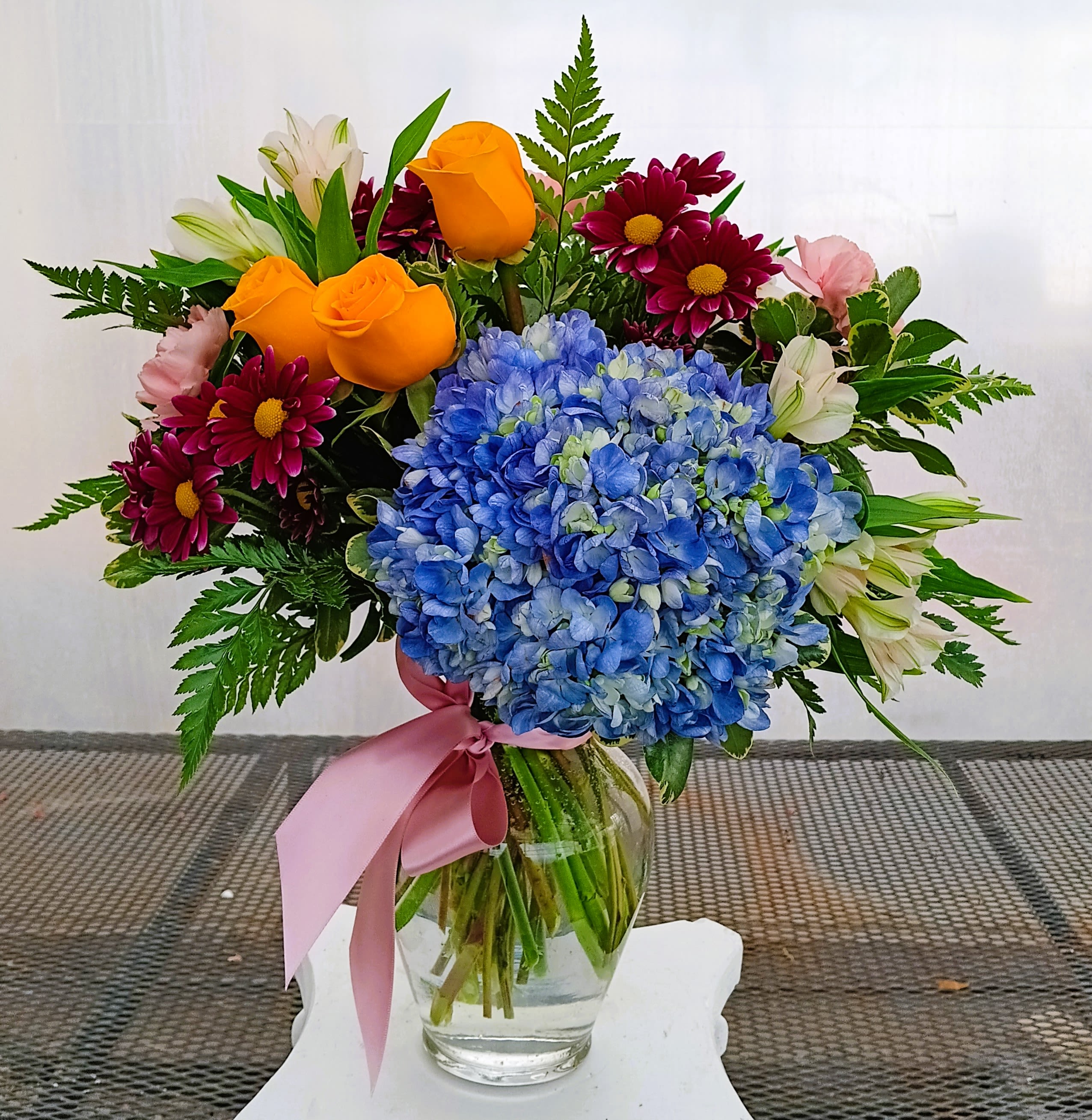 Springtime Waltz  - Step into the rhythm of spring with this enchanting arrangement, where each bloom tells a story of grace and renewal. Lush blue hydrangeas form a dreamy backdrop, evoking the calm serenity of clear skies. Elegant roses dance gracefully alongside cheerful daisies that bring a touch of playful charm. Delicate alstroemeria weave through the design, adding whispers of sophistication, while vibrant carnations provide a lively pop of color. Together, these blooms create a harmonious symphony, perfect for celebrating life’s most beautiful moments. Let Springtime Waltz brighten your space and heart with its timeless elegance.  Please be advised that the florist will fulfill the order to its full value using the freshest flowers available in stock. If necessary, substitutions will be made for similar flowers and colors to maintain the intended vision of the arrangement.