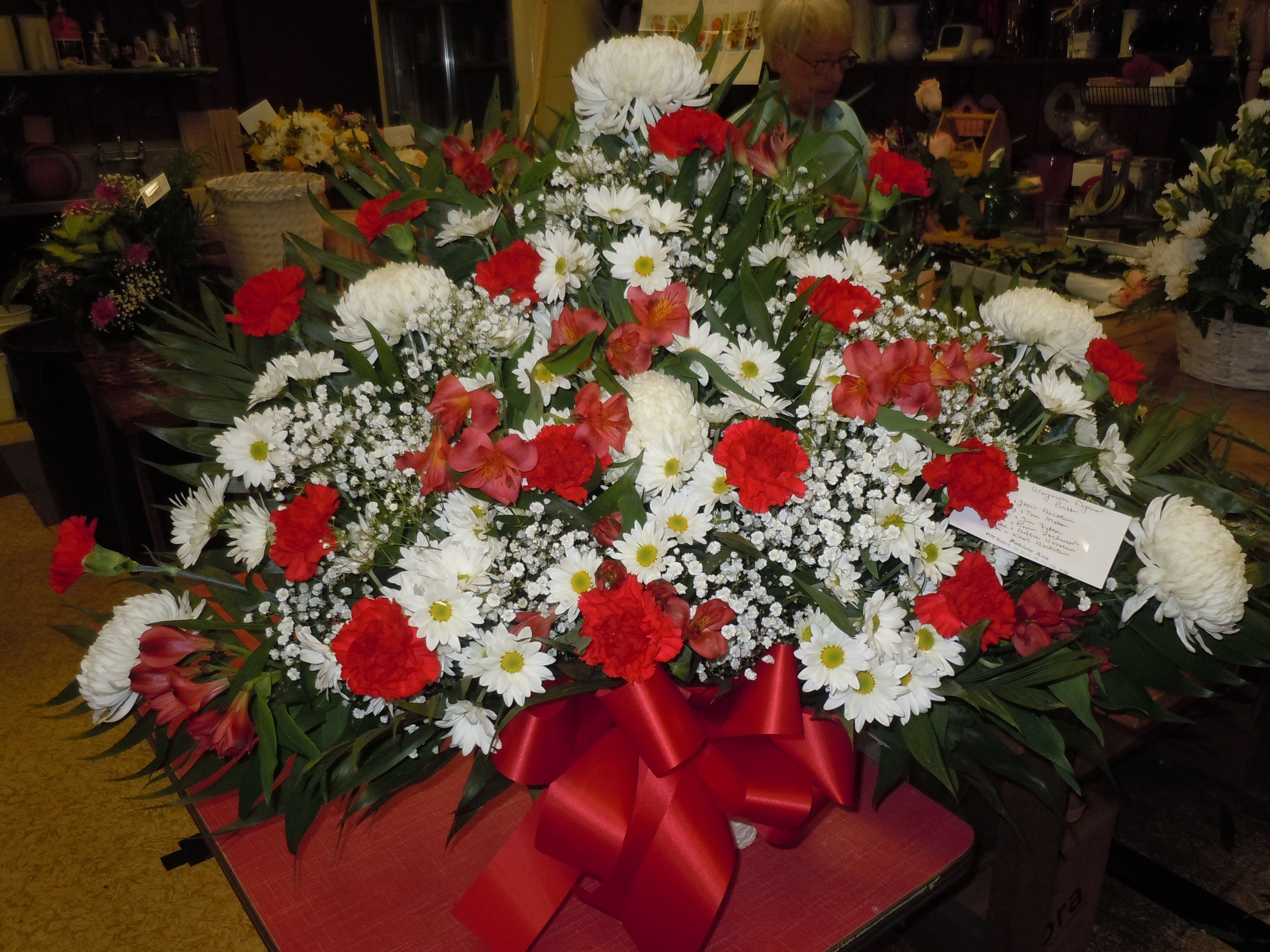 TB1 Sympathy Basket - Sympathy mache - includes white spider mums, white daisies, red carnations, red alstromaria, baby's breath, greens, and bow.  Banners not included $15 + per banner   Substitutions may apply pending flower availibilty
