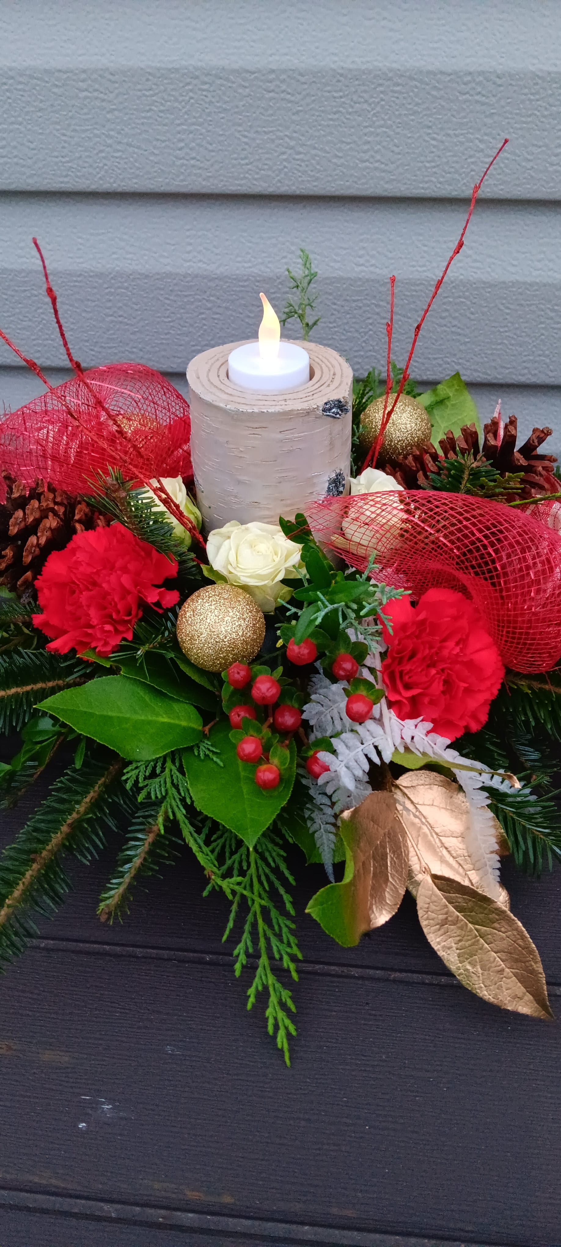 Christmas Wishes Centerpiece  - Round holiday  centerpiece with faux birch candle holder, red carnations, spray roses, greenery. Deluxe and premium will include roses.