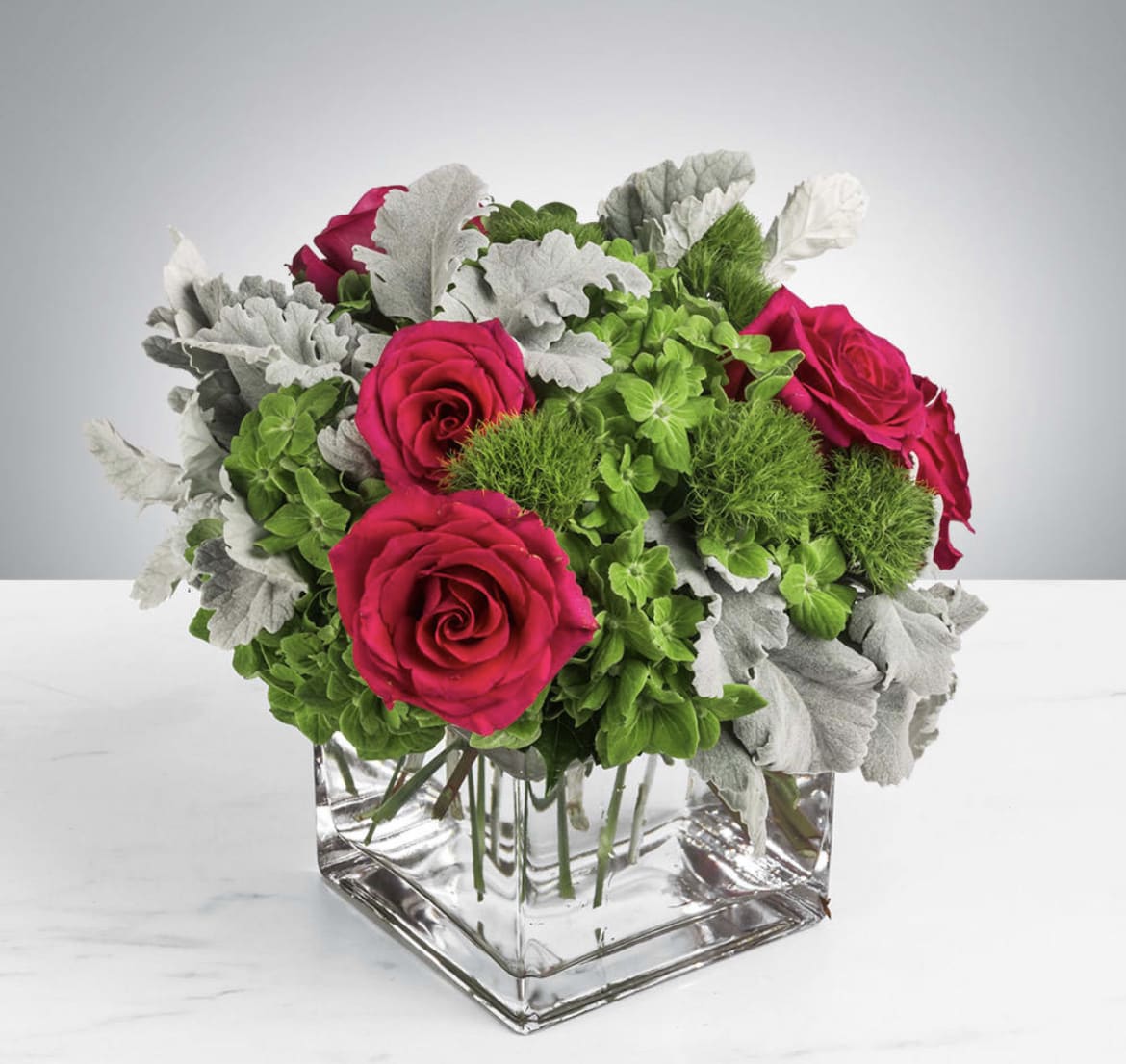 In Bloom - This arrangement includes hot pink roses, green hydrangea, green dianthus, dusty miller. In Bloom is the perfect gift to wish someone a happy birthday or to say thank you. APPROXIMATE DIMENSIONS: 12&quot; H X 10&quot;W