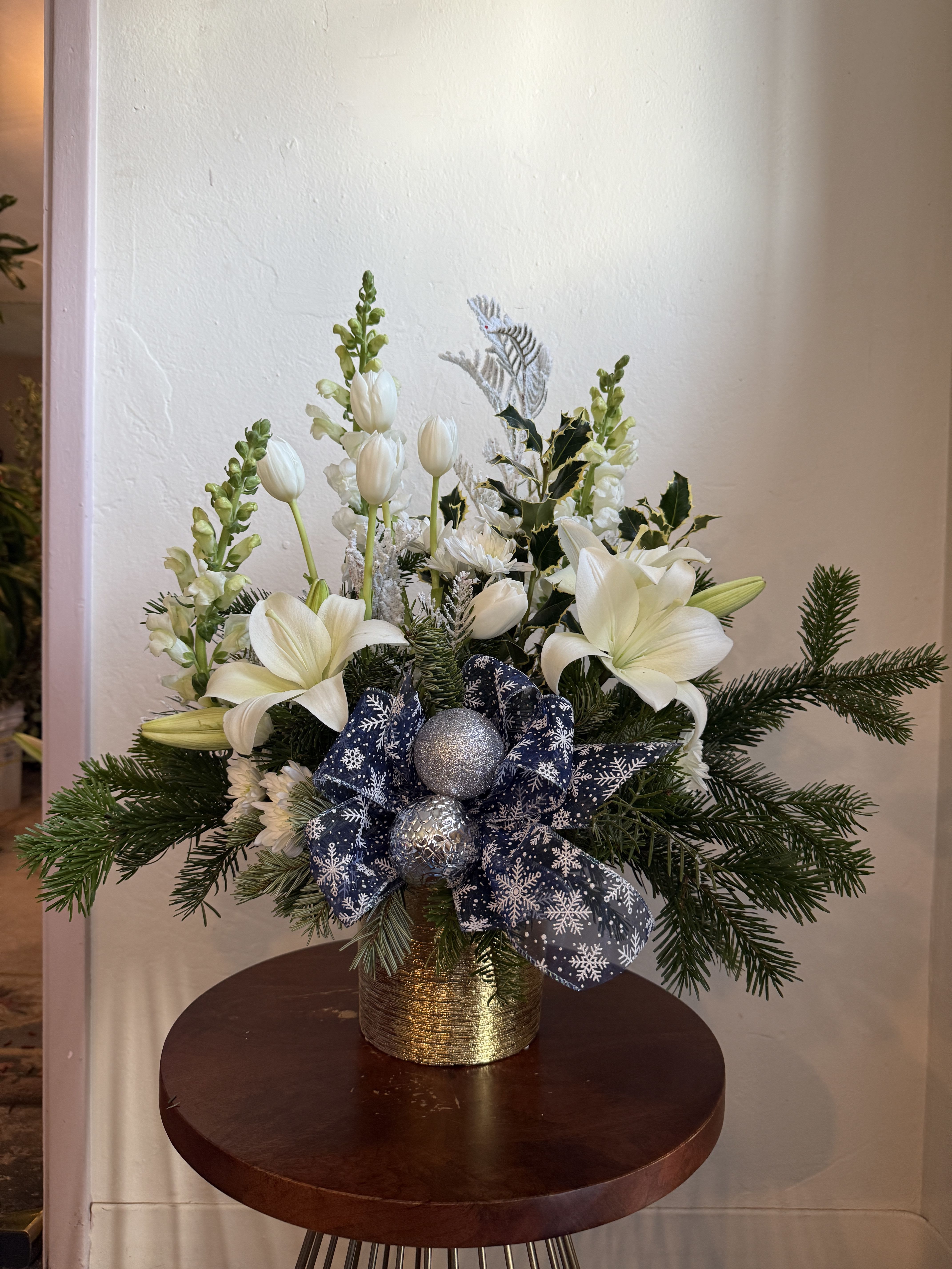 Frosted Holiday Arrangment - A variety of blooms including lilies, tulips, snapdragons and winter greens. Ornaments and ribbon included.