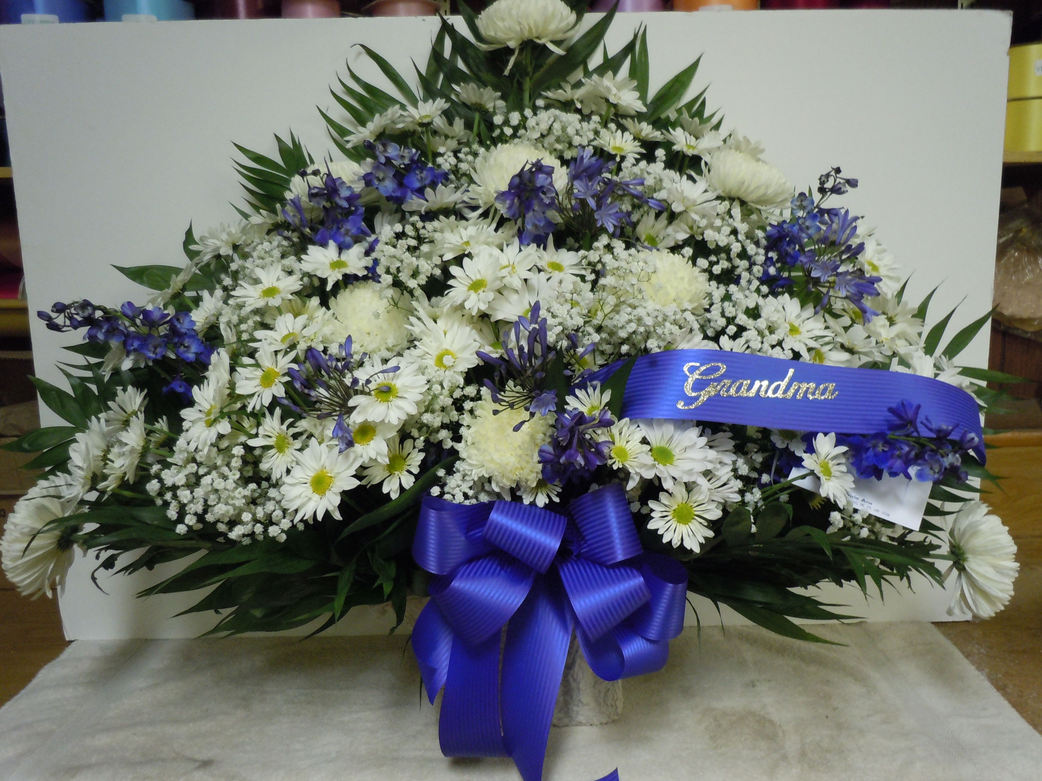 TB9 Traditional Basket - Sympathy mache - includes white spider mums, white daisies, dark blue delphinium, baby's breath, greens, and bow.  Banners not included $15 + per banner   Substitutions may apply pending flower availibilty