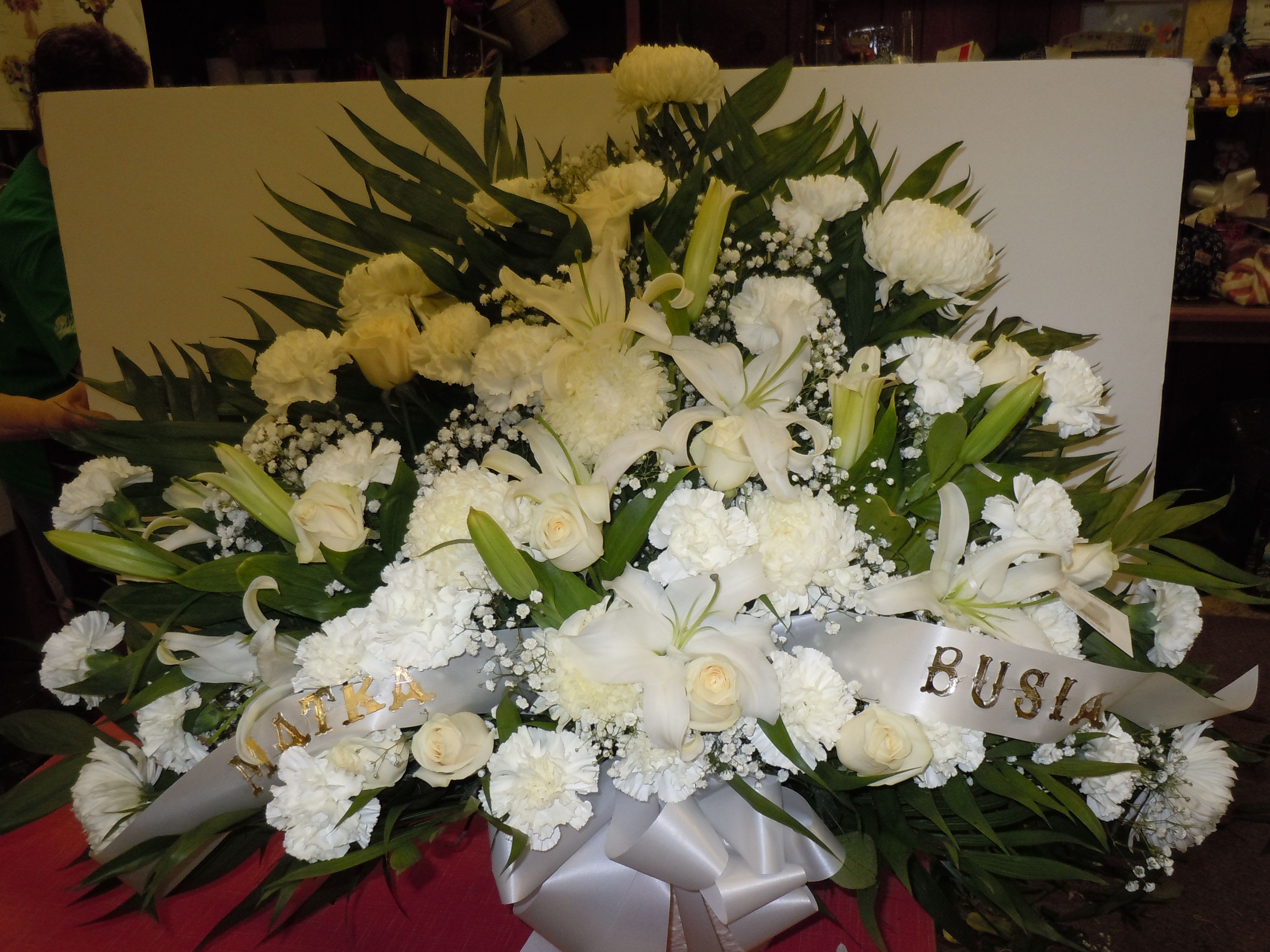 TB10 Traditional Basket - Sympathy mache - includes white spider mums, white oriental lilies, white carnations, white roses, baby's breath, greens, and bow.   Banners not included $15 + per banner   Substitutions may apply pending flower availibilty