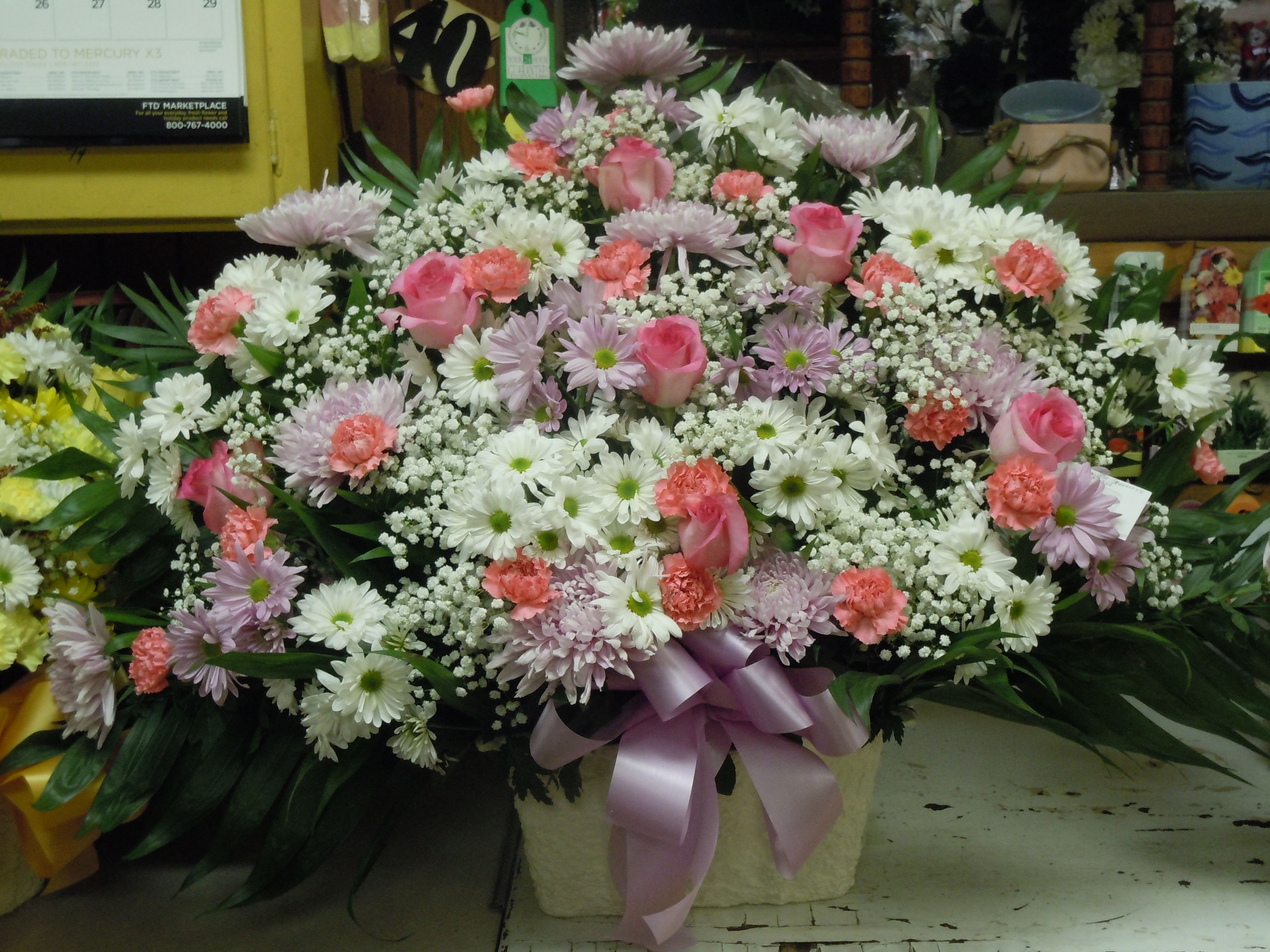 TB15 Traditional Basket - A mixture of white and lavender daisies, pink carnations, pink roses, lavender fuji mums, baby's breath, greens and lavender bow  Banner - $15.00 + extra  Substitutions may apply due to flower availability
