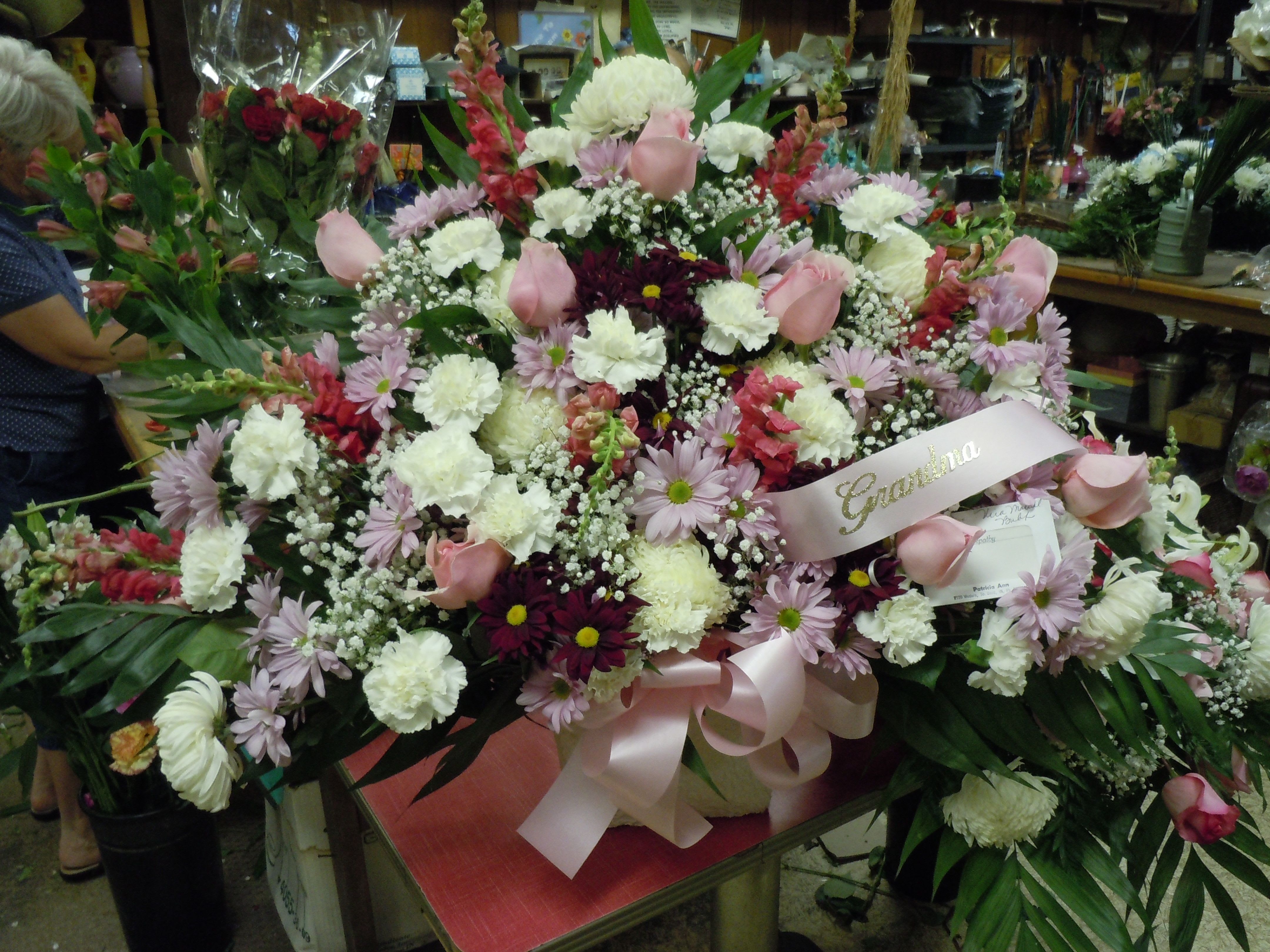 TB16 Traditional Basket - A mixture of burgandy and lavender daisies, white carnations, lavender roses, white fuji mums, fark pink snaps, baby's breath, greens and lavender bow   Banner - $15.00 + extra  Substitutions may apply due to flower availability