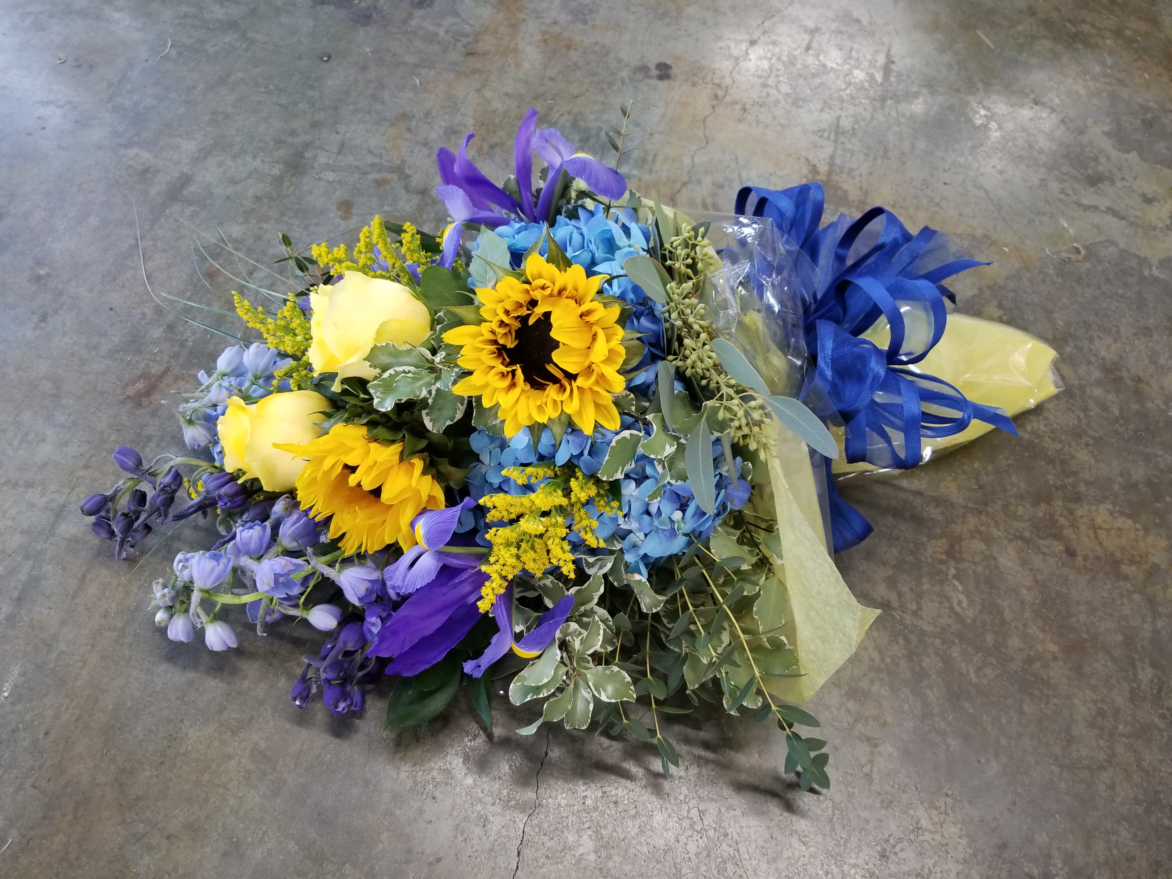 Graduation Cello - Select this festive blue and yellow combination of flowers beautiful wrapped in cellophane. Flowers include hydrangea, roses, iris and belladonna.