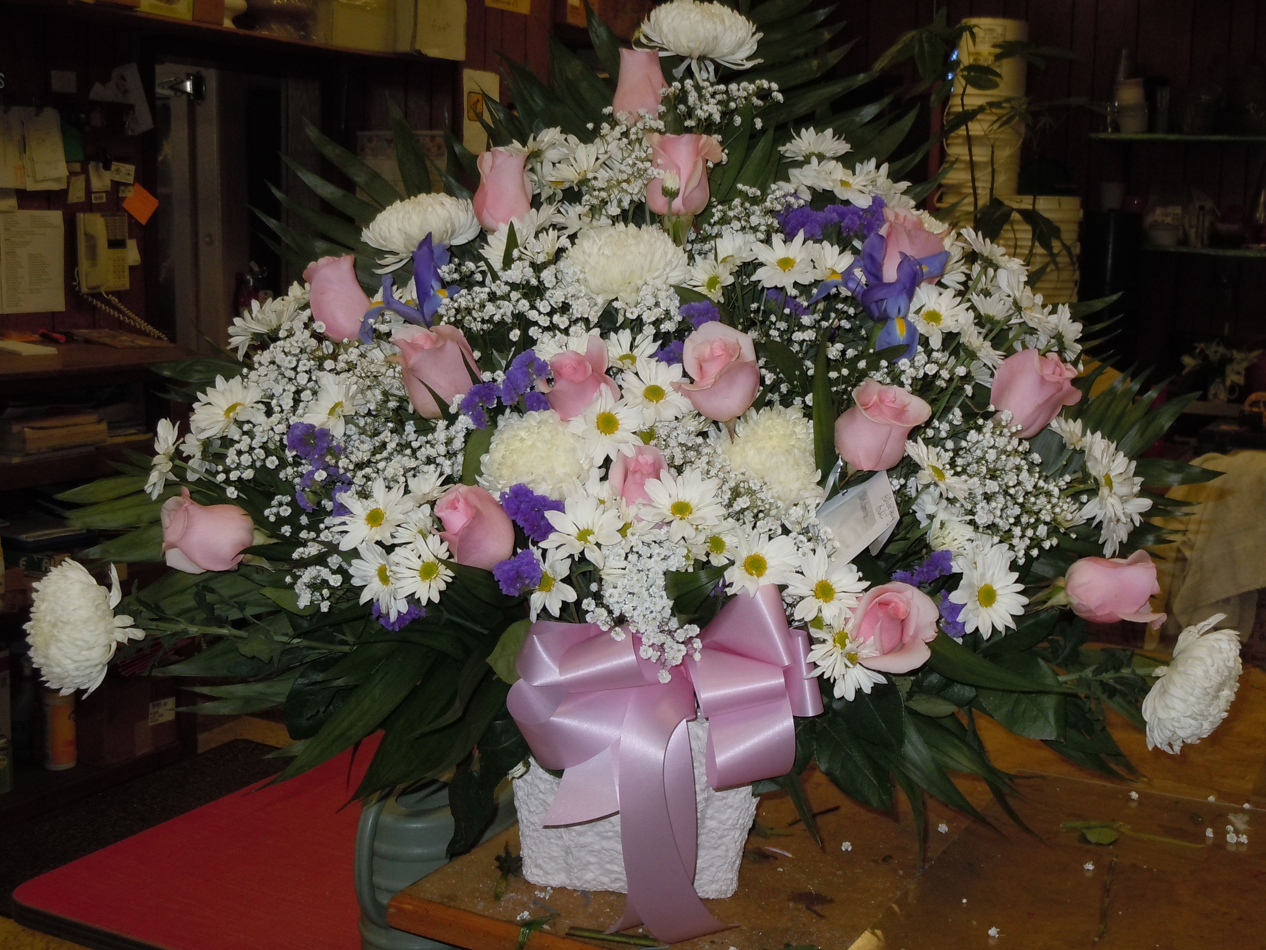TB17 Traditional Basket - A mixture of white daisies, pink carnations, pink roses, white fuji mums, baby's blue iris, breath, greens and lavender bow   Banner - $15.00 + extra  Substitutions may apply due to flower availability