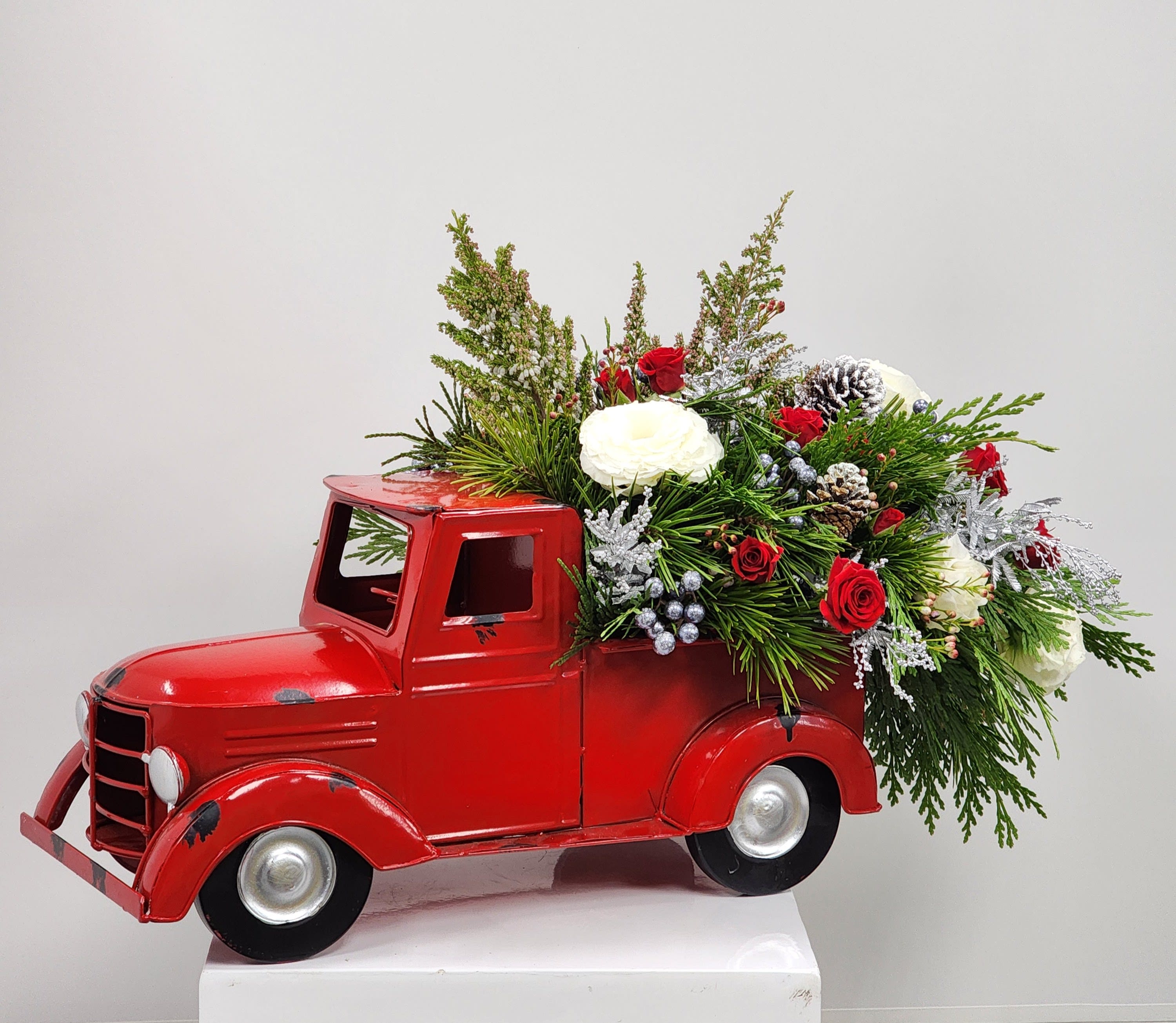 Holiday Haul - Select this dashing container driving with an arrangement in the truck bed. Filled with spray roses, lisianthus, heather, pinecones, and accented with wax flower.  Approximately 15&quot; tall by 13&quot; wide and 23&quot; long.