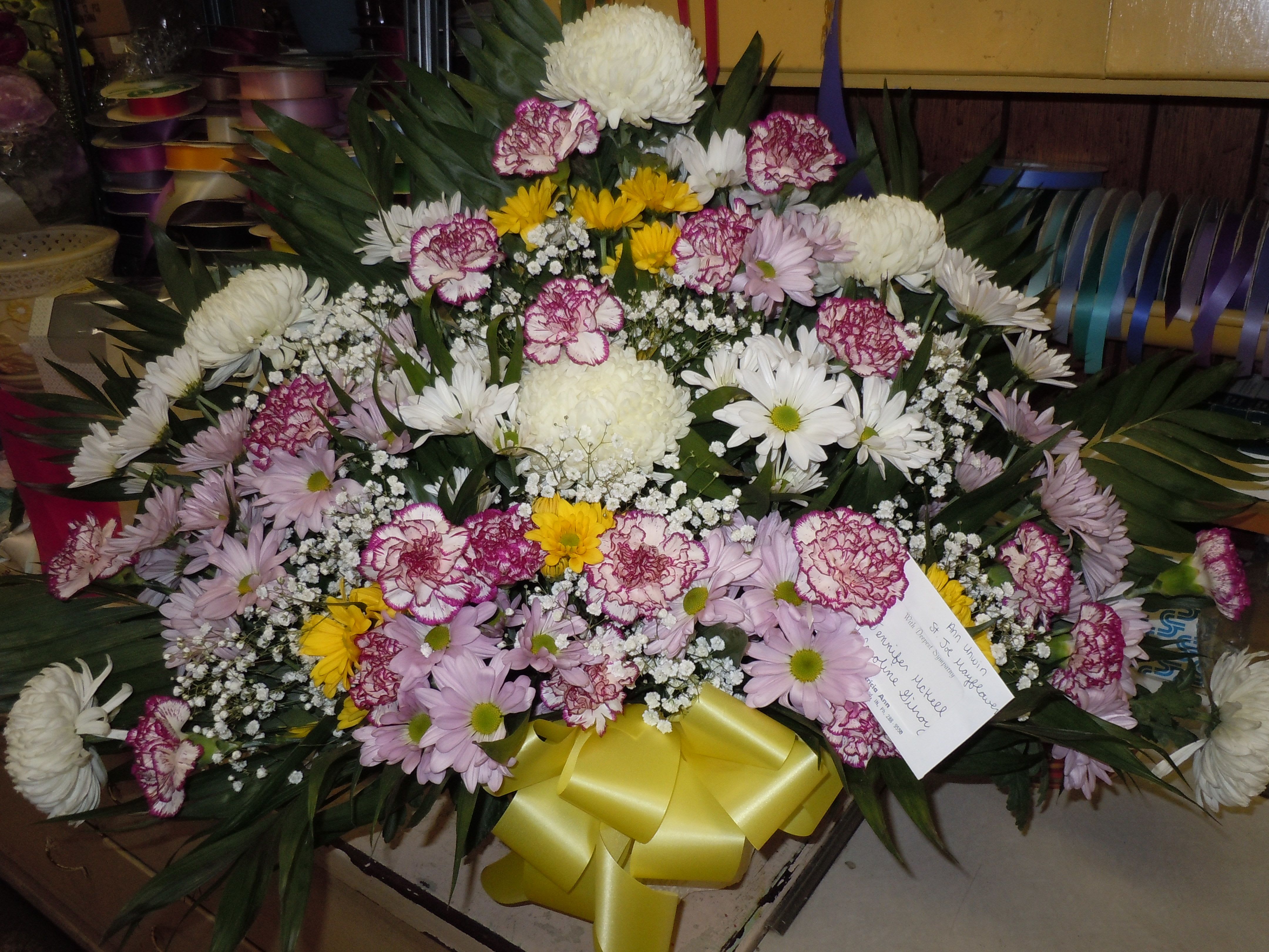 TB18 Traditional Basket - A mixture of white, lavender and yellow daisies, purple tipped carnations, white fuji mums, baby's breath, greens and yellow bow  Banner - $15.00 + extra  Substitutions may apply due to flower availability