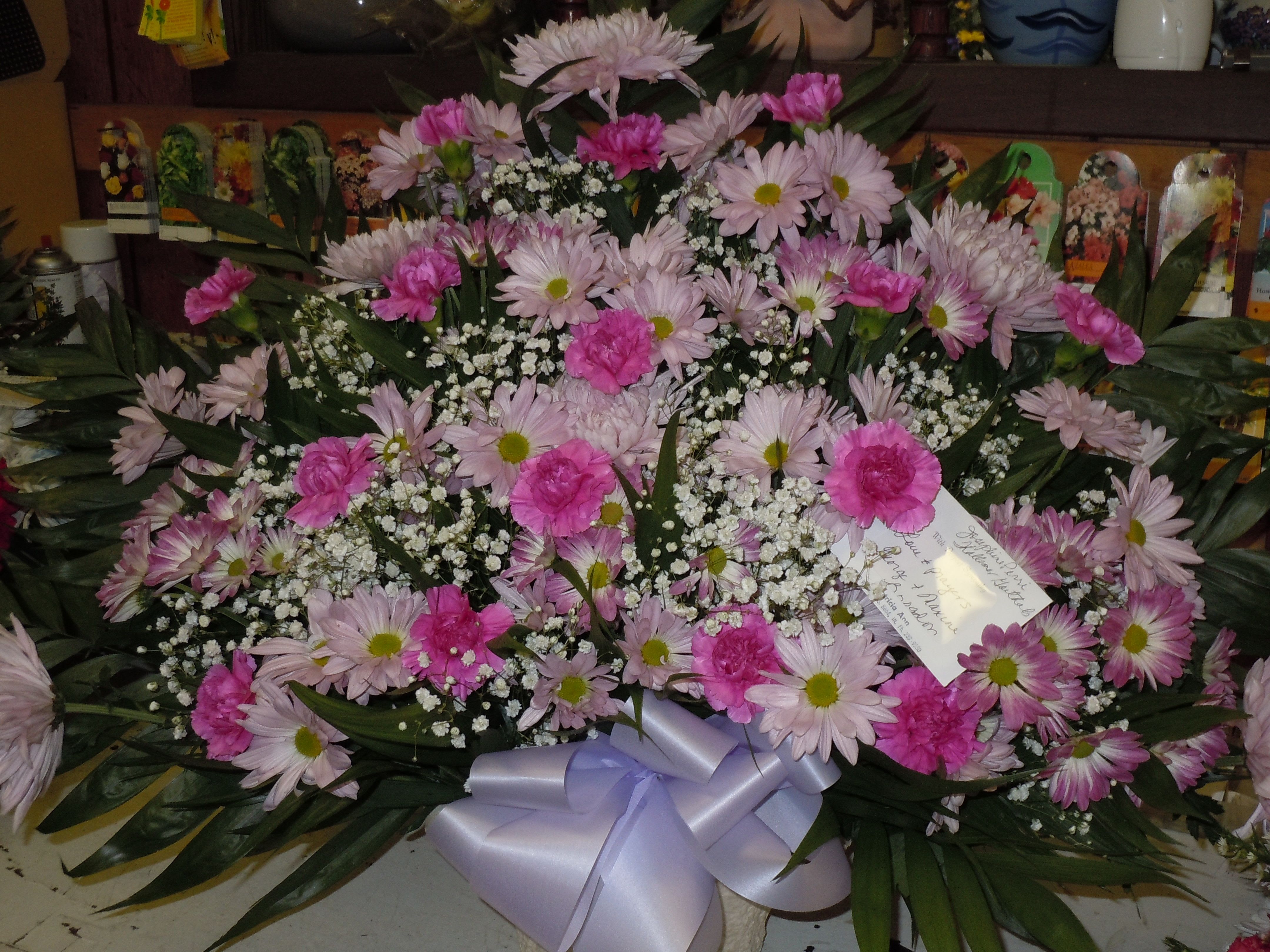 TB19 Traditional Basket - A mixture of lavender and purple edged daisies,  orchid pink carnations, lavender fuji mums, baby's breath, greens and lavender bow  Banner - $15.00 + extra  Substitutions may apply due to flower availability