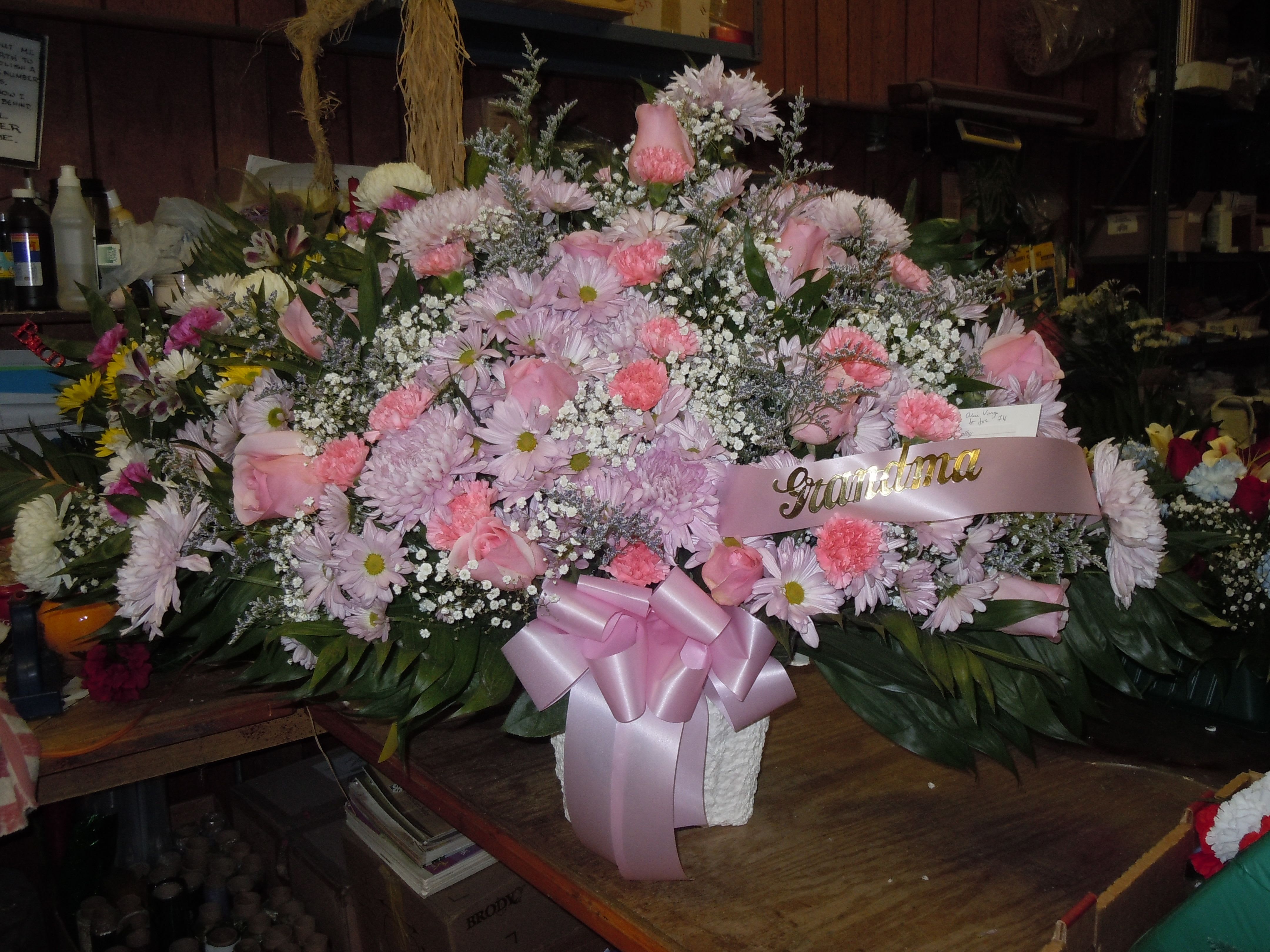 TB20 Traditional Basket - A mixture of lavender daisies, pink carnations, pink roses, lavender fuji mums, baby's breath, greens and pink bow   Banner - $15.00 + extra  Substitutions may apply due to flower availability