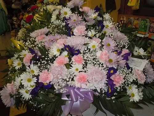 TB21 Traditional Basket - A mixture of white and lavender daisies, pink carnations, purple/blue iris, lavender fuji mums, baby's breath, greens and lavender bow   Banner - $15.00 + extra  Substitutions may apply due to flower availability