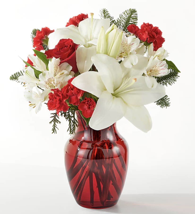 Holiday Season Bouquet - This radiant Red Stunner bouquet is designed to spread joy and holiday cheer all season long. Filled with lush red blooms and festive accents, it makes a heartfelt and elegant gift for anyone celebrating the magic of Christmas   Details The Deluxe Bouquet is approximately 15"H x 13"W. Designed by florists, ready to display. For long–lasting blooms, replace the water daily. We suggest trimming the stems every couple days. Pet Safety Precautions: This bouquet or plant may include flowers and foliage that are known to be toxic to pets. To keep them safe, be sure to keep this arrangement out of your pet's reach.   Bloom Details Carnation Alstroemeria Rose Lily Christmas Greens 