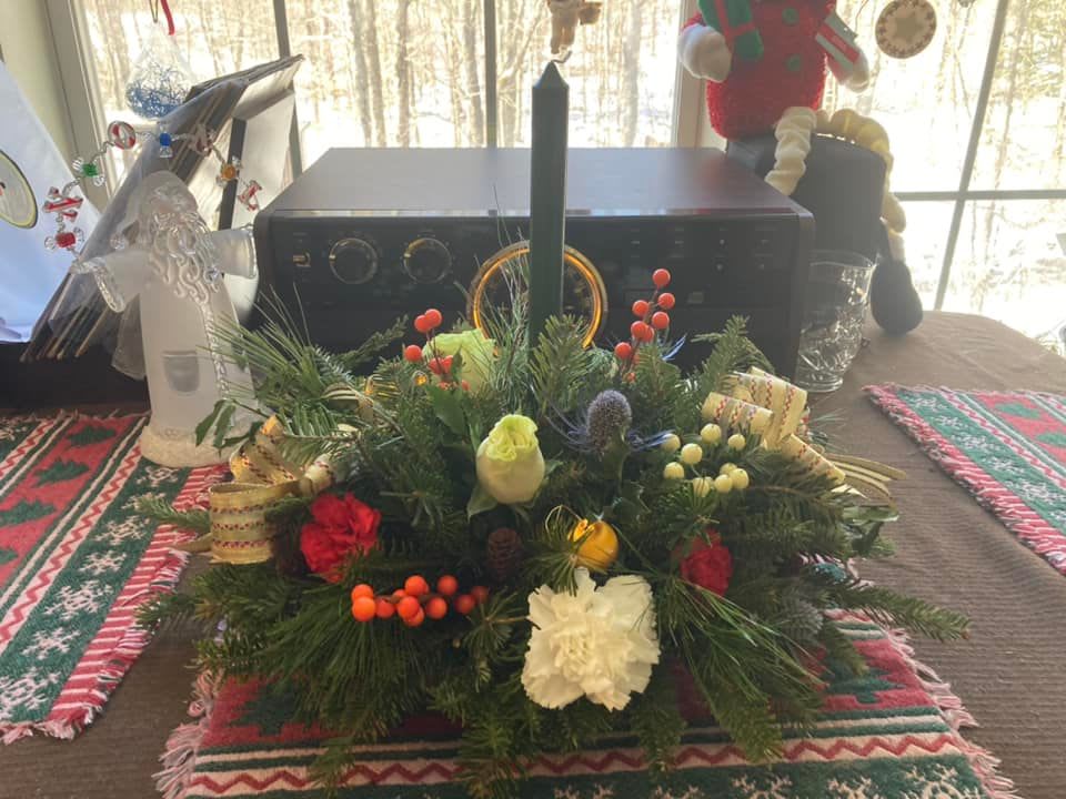 Traditional Christmas Table Centerpiece - Standard Price - Includes a single candle centerpiece, filled with beautiful Flowers, Festive decor and a mix of winter Greens. Deluxe Price - Includes two candles centerpiece, filled with more flowers, festive decor and a mix of winter Greens.