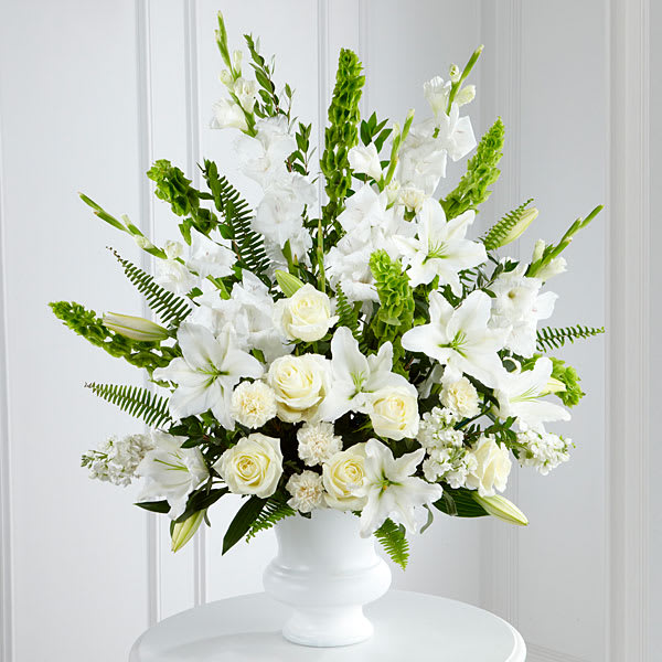 Morning Stars Arrangement - Morning Stars™ Arrangement is a brilliant expression of peace and soft serenity. White roses carnations gladiolus stock and Oriental lilies are accented with the bright green stems of Bells of Ireland and a gorgeous assortment of lush greens while seated in a white designer plastic urn to create a beautiful way to honor the life of the deceased.