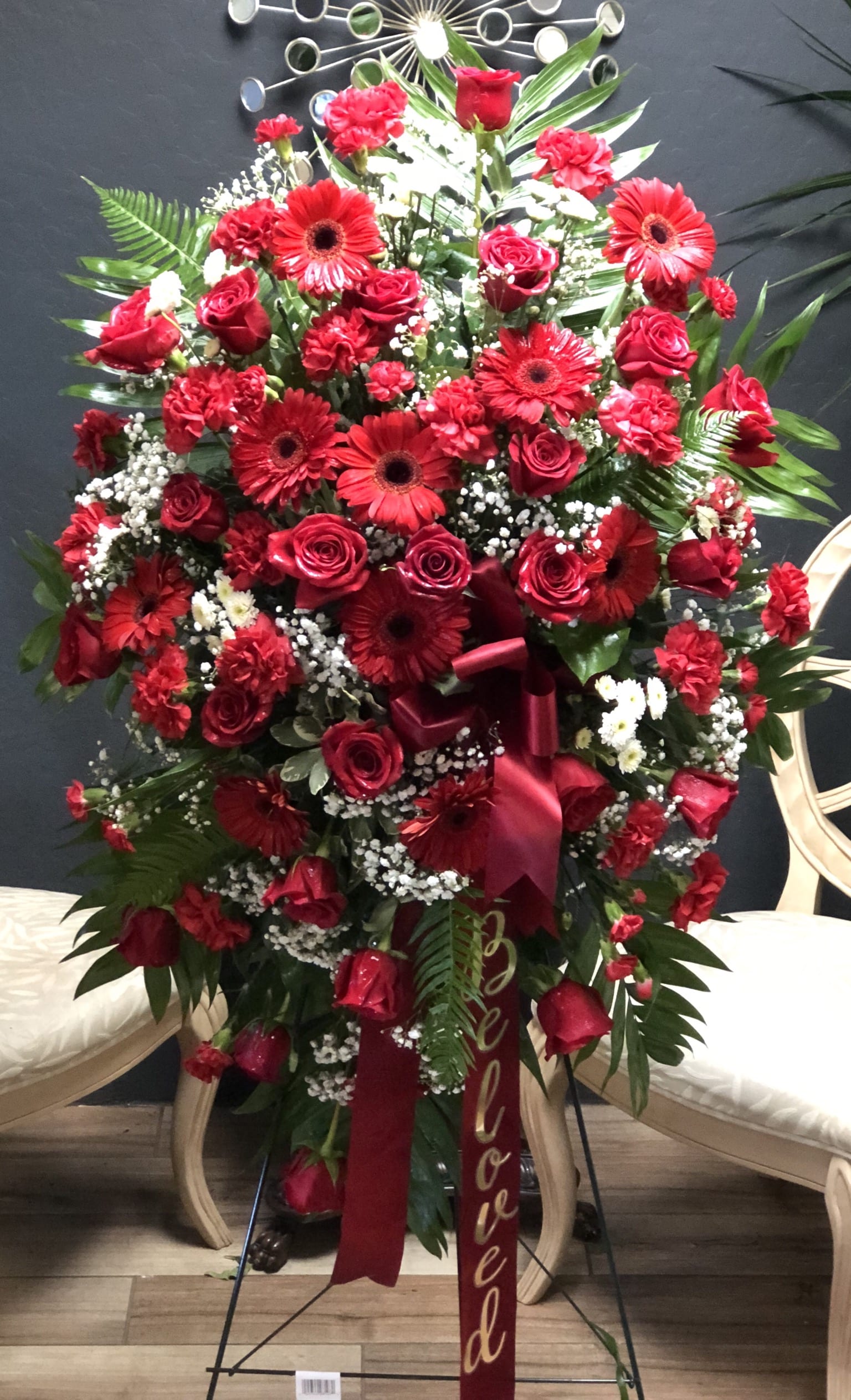 The FTD Treasured Memories Standing Spray - The FTD® Treasured Memories™ Standing Spray is a rich and colorful way to express your unending love and devotion to the departed. An exceptional arrangement of red roses burgundy carnations burgundy mini carnations red gerbera daisies and white button poms are accented with a variety of lush greens. A red ribbon with the word &quot;Beloved &quot; embossed in a gold metallic lettering finishes this beautiful display for their final farewell service. Displayed on a wire easel.