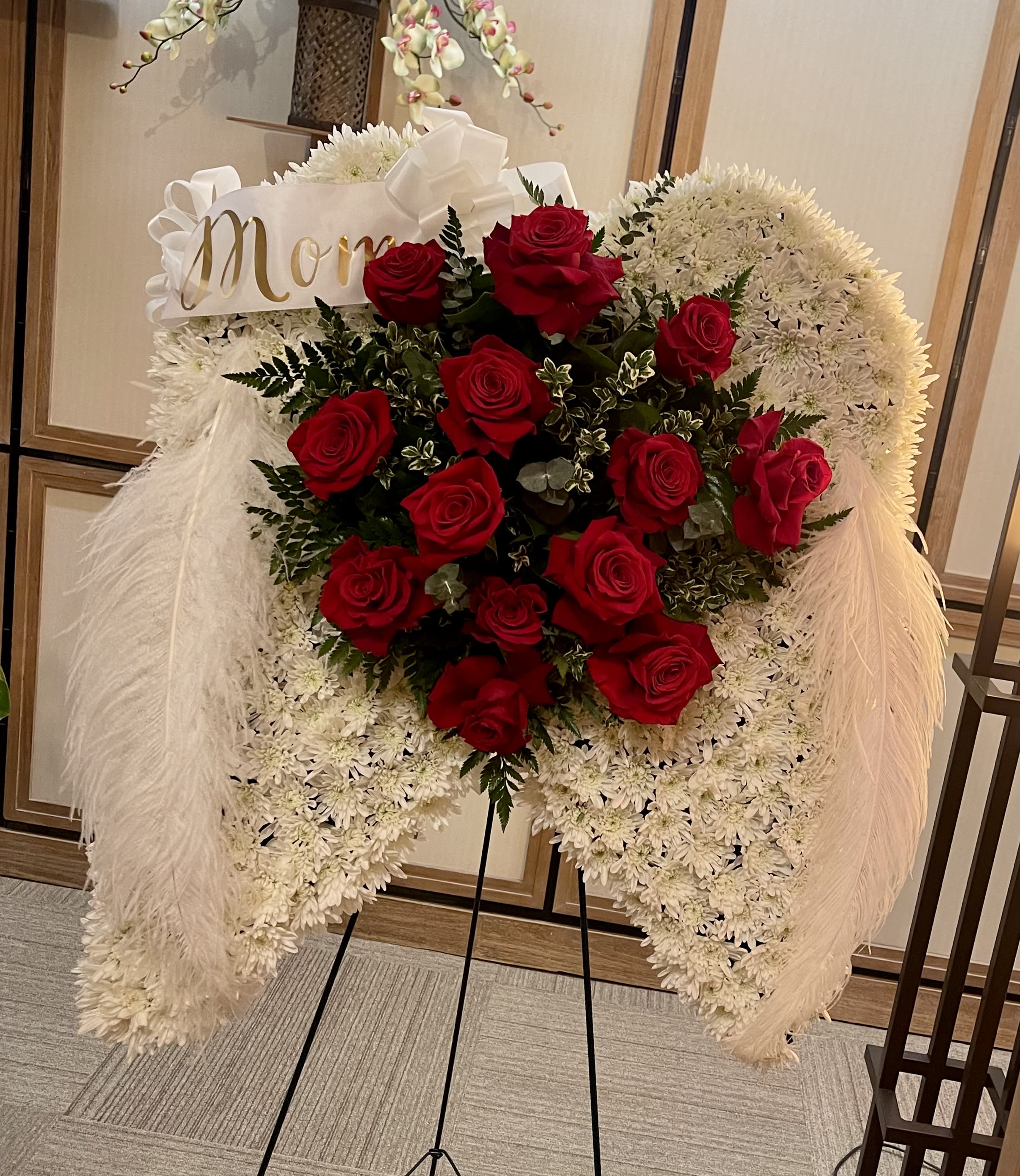 Angel Wings Standing Spray - When your feelings of loss and sorrow compel you to make a grand gesture of sympathy this dramatic standing arrangement is a lovely way to convey your sincerest condolences. This extraordinary composition of white blooms and red roses handcrafted by artisan florist. Made to be displayed on an easel it makes an appropriate choice for a wake funeral or graveside service sure to be much appreciated and long remembered. Standard Base Size 18in wide x 24in long  