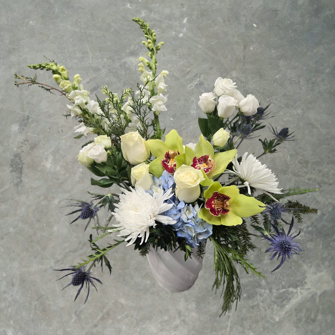 Arctic Garden  - Arctic Garden  Designed in a sleek white pot, it’s overflowing with customer favorites: blue, white, and green hydrangea, elegant roses, airy lisianthus, snapdragons, and premium orchids. Accented with eucalyptus and seasonal winter greens, this lush design delivers beauty, texture, and unforgettable impact. 