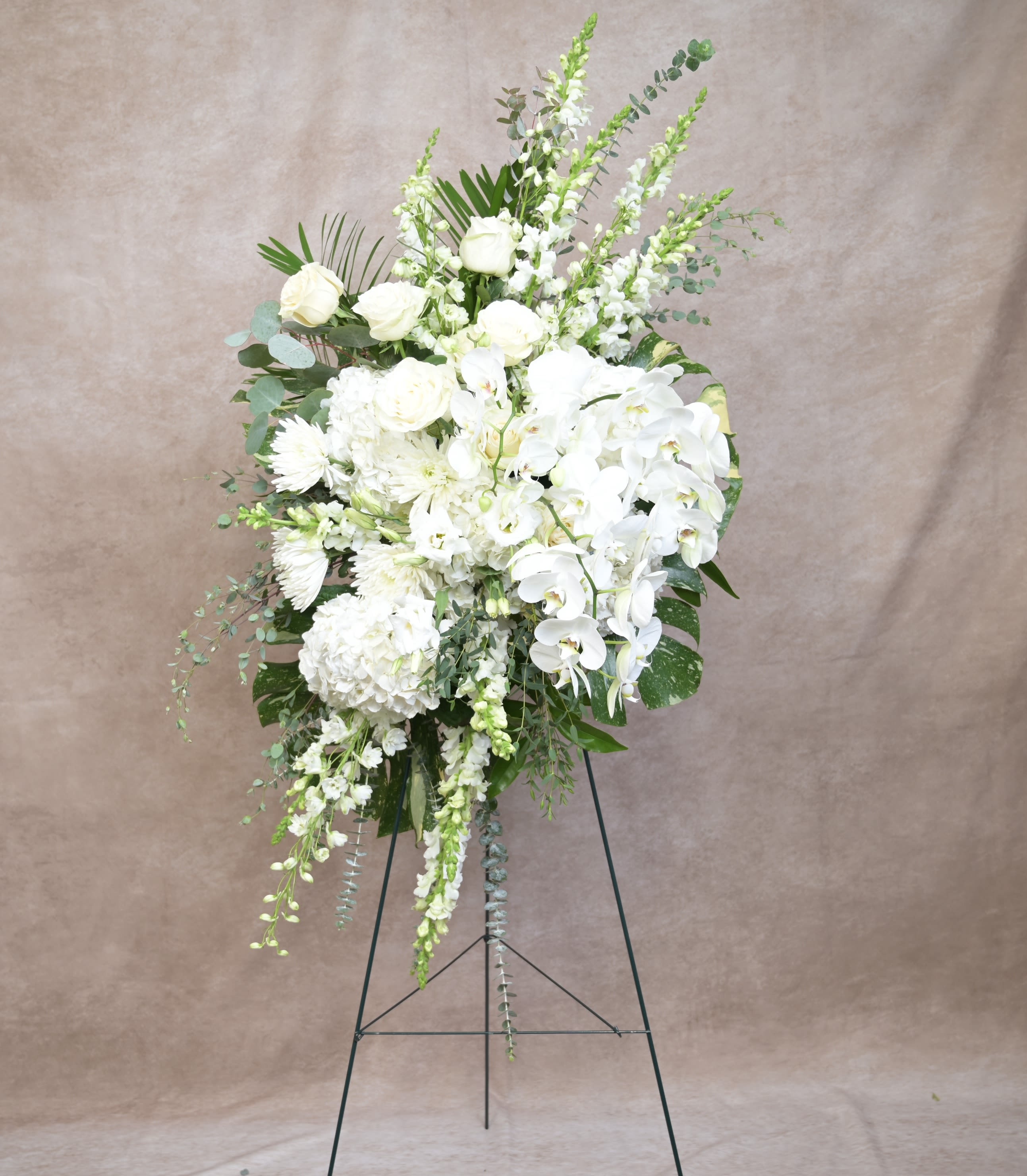  Eternal Grace - Eternal Grace Elegant, serene, and profoundly heartfelt, Eternal Grace offers a timeless expression of love and remembrance. This standing spray features an abundant blend of soft white blooms arranged in a sweeping, garden-style composition that feels peaceful, refined, and full of quiet beauty. Gentle movement, layered textures, and natural greenery create a sense of purity and calm, making this tribute a meaningful presence at any service or celebration of life. Please Note: Our arrangements are handcrafted, and no two pieces are ever identical. Variations in flower types, color tones, and exact placement will occur based on daily availability. We do not create factory-duplicate designs — instead, we recreate the style, palette, and overall feel of the arrangement while ensuring every piece is fresh, beautiful, and premium.