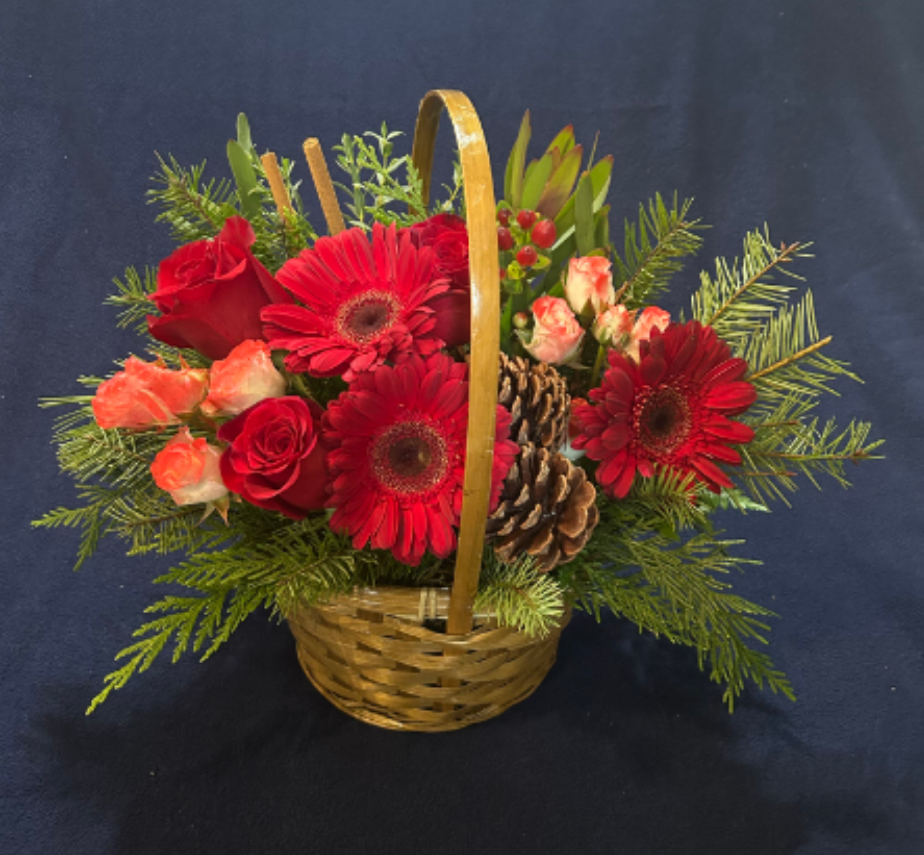 Joy in Holidays  - A warm celebration of nature’s bounty, this arrangement blends crimson roses, gerberas, pinecones, and berries in a rustic basket. It evokes the charm of winter gatherings and the joy of giving, wrapped in seasonal greenery and heartfelt color.