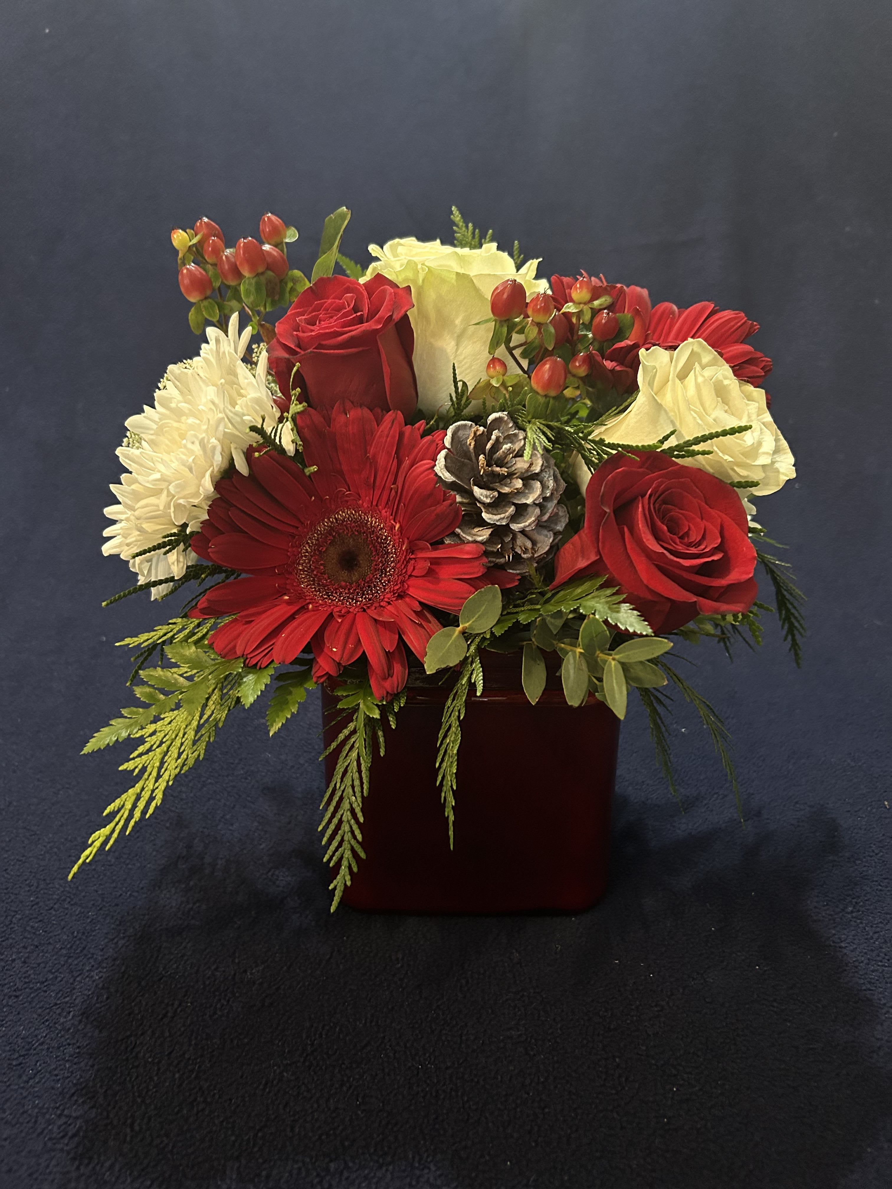 Radiant dawn of Christmas - A festive blend of red roses, white blooms, gerberas, pinecones, and berries arranged in a deep red vase. This centerpiece evokes the warmth of Christmas and the elegance of winter, perfect for holiday tables or heartfelt gifts.