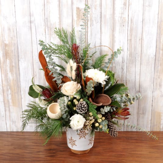 Snow - Beautiful neutral arrangement full of mixed wintergreens, natural items, roses,  mums, safari sunset and pinecones in a keepsake white snowflake container.
