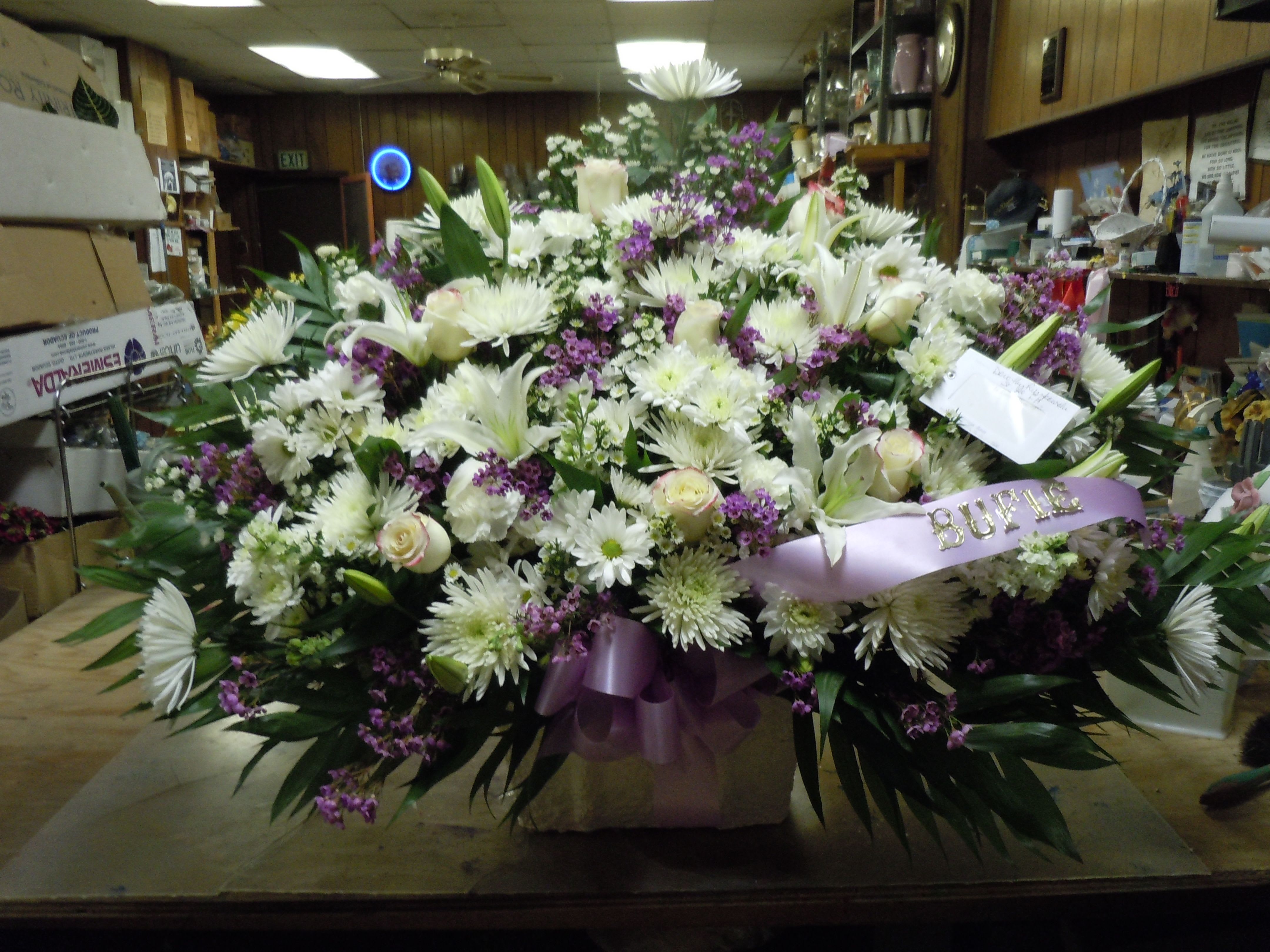 TB23 Sympathy Basket - A mixture of white daisies, white carnations, white roses, white fuji mums, baby's breath, greens and lavender bow bow   Banner - $15.00 + extra  Substitutions may apply due to flower availability