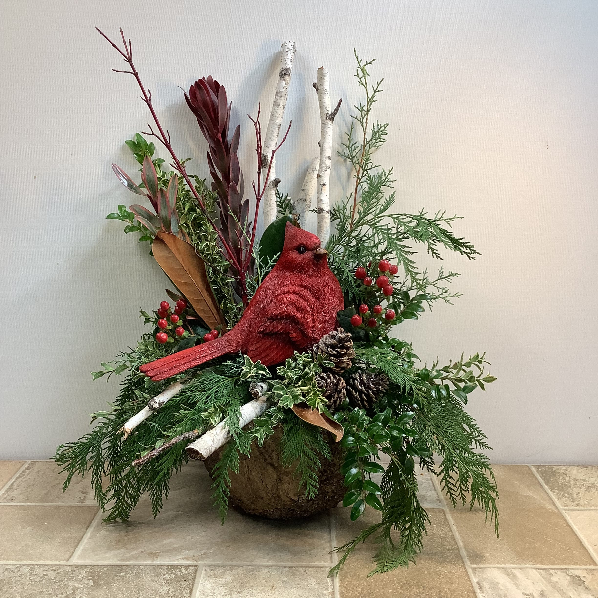 Woodland Beauty - This beautiful arrangement makes a lovely gift for many occasions. Every detail has been carefully thought out to make it a memorable offering. It features fresh evergreens, red hypericum berries, magnolia leaves, birch branches, pine cones and a pretty cardinal in a bark-like resin pot. It’s a good sized piece measuring 14” wide x 20” tall.  Flower delivery La Crosse, Onalaska, Holmen, West Salem, La Crescent. Flower shop. Plant store. Best florist La Crosse Wisconsin area.  Seasonal and holiday floral creations. Funeral arrangements. New baby bouquets. Birthday celebration flowers. Get well arrangements. Just because gifts.