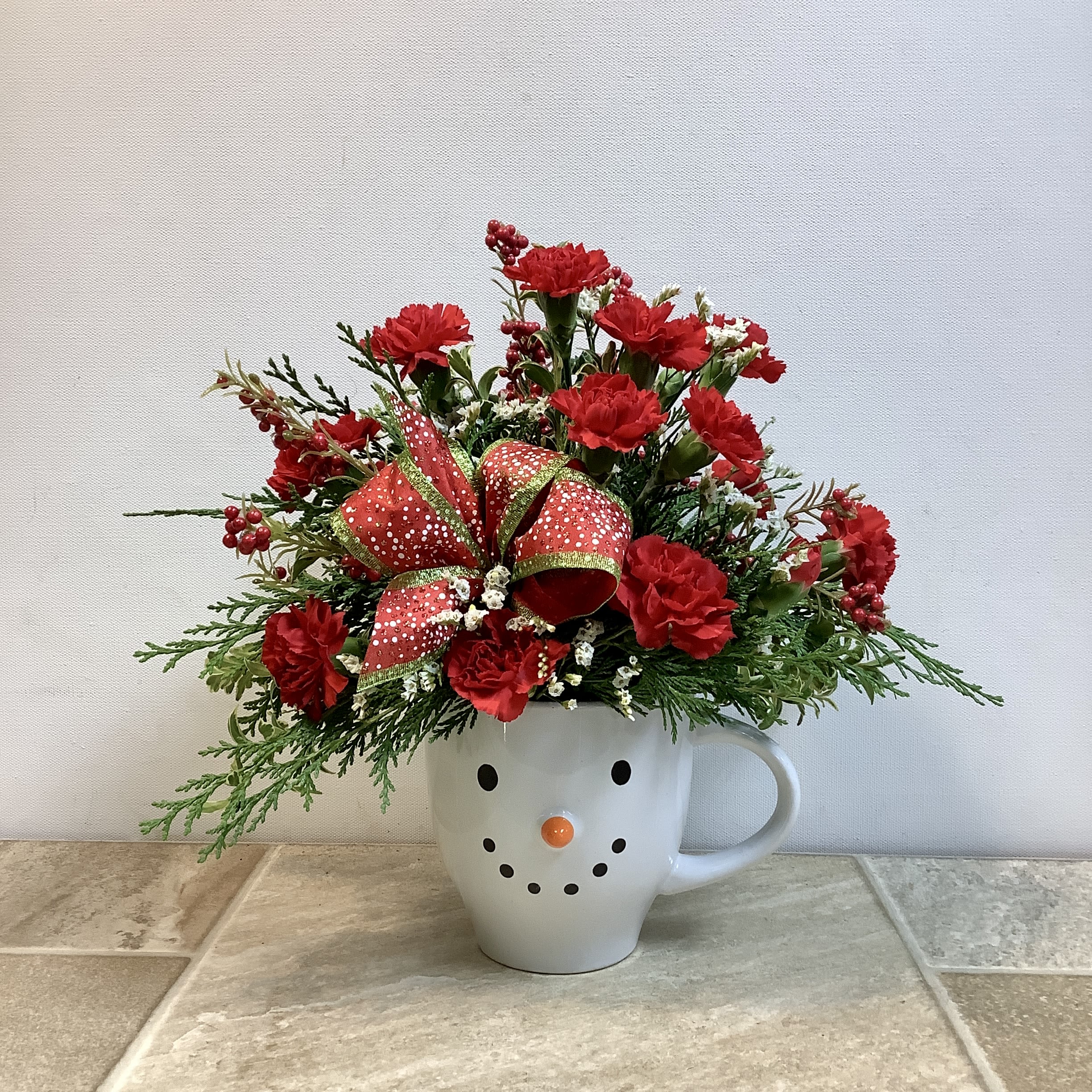 Berry Cute Snowman - Celebrate winter with our happy Berry Cute snowman mug, filled with fresh evergreens, red mini carnations, white limon and red silk berries. Accented with a festive bow, this cheerful and long-lasting arrangement will bring a smile to anyone's face! Approximate size: 12” x 12”.   Primary flower: carnation  Flower delivery La Crosse, Onalaska, Holmen, West Salem, La Crescent. Flower shop. Plant store. Best florist La Crosse Wisconsin area.  Seasonal and holiday floral creations. Funeral arrangements. New baby bouquets. Birthday celebration flowers. Get well arrangements. Just because gifts.