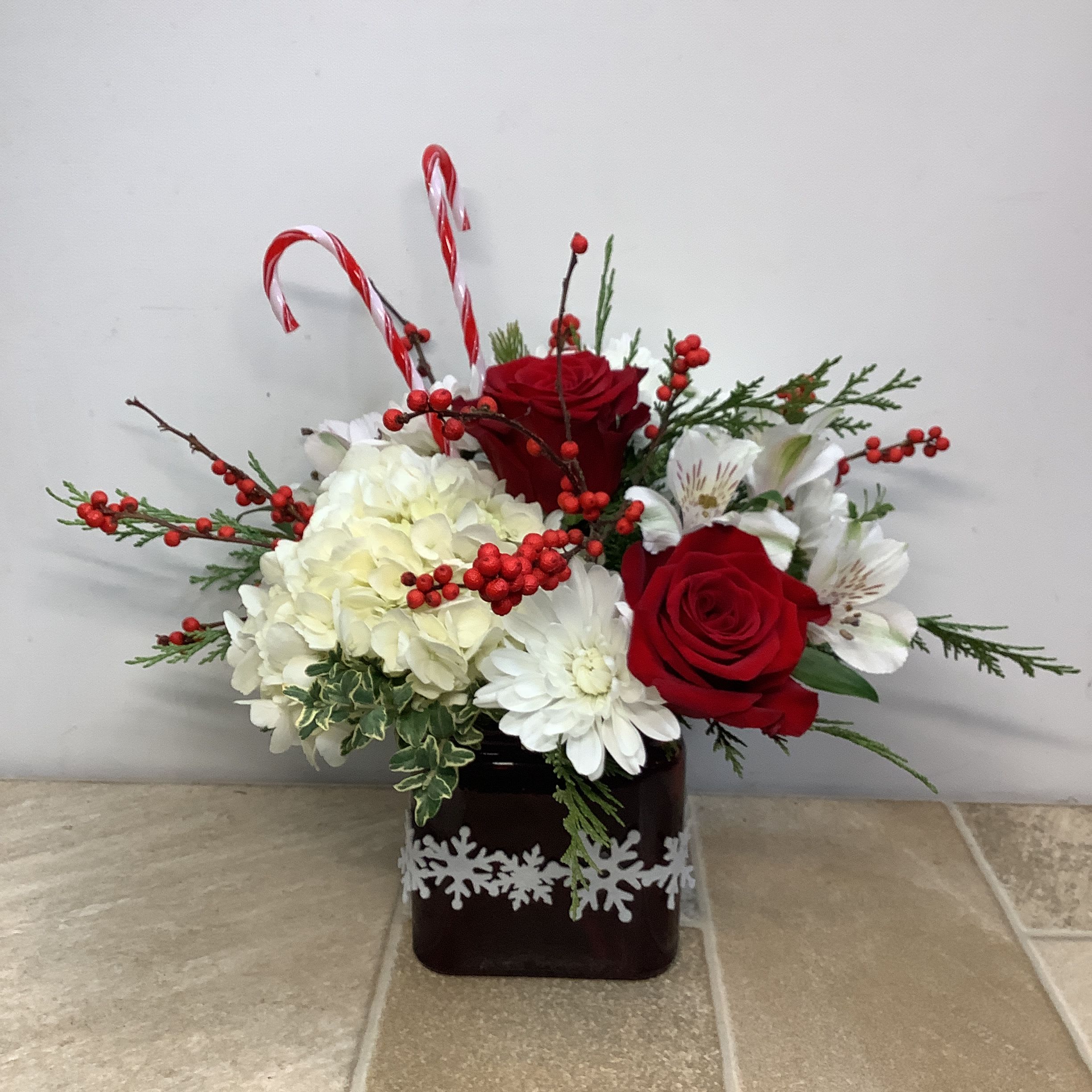 Holiday Magic - This magical bouquet is filled to the brim with white hydrangeas, chrysanthemums and alstroemeria along with red roses and winterberry. Plastic candy canes add a fun, festive touch. Approximate size: 14” wide x 14” tall.  Primary flowers: hydrangea, mum, lily  Flower delivery La Crosse, Onalaska, Holmen, West Salem, La Crescent. Flower shop. Plant store. Best florist La Crosse Wisconsin area.  Seasonal and holiday floral creations. Funeral arrangements. New baby bouquets. Birthday celebration flowers. Get well arrangements. Just because gifts.
