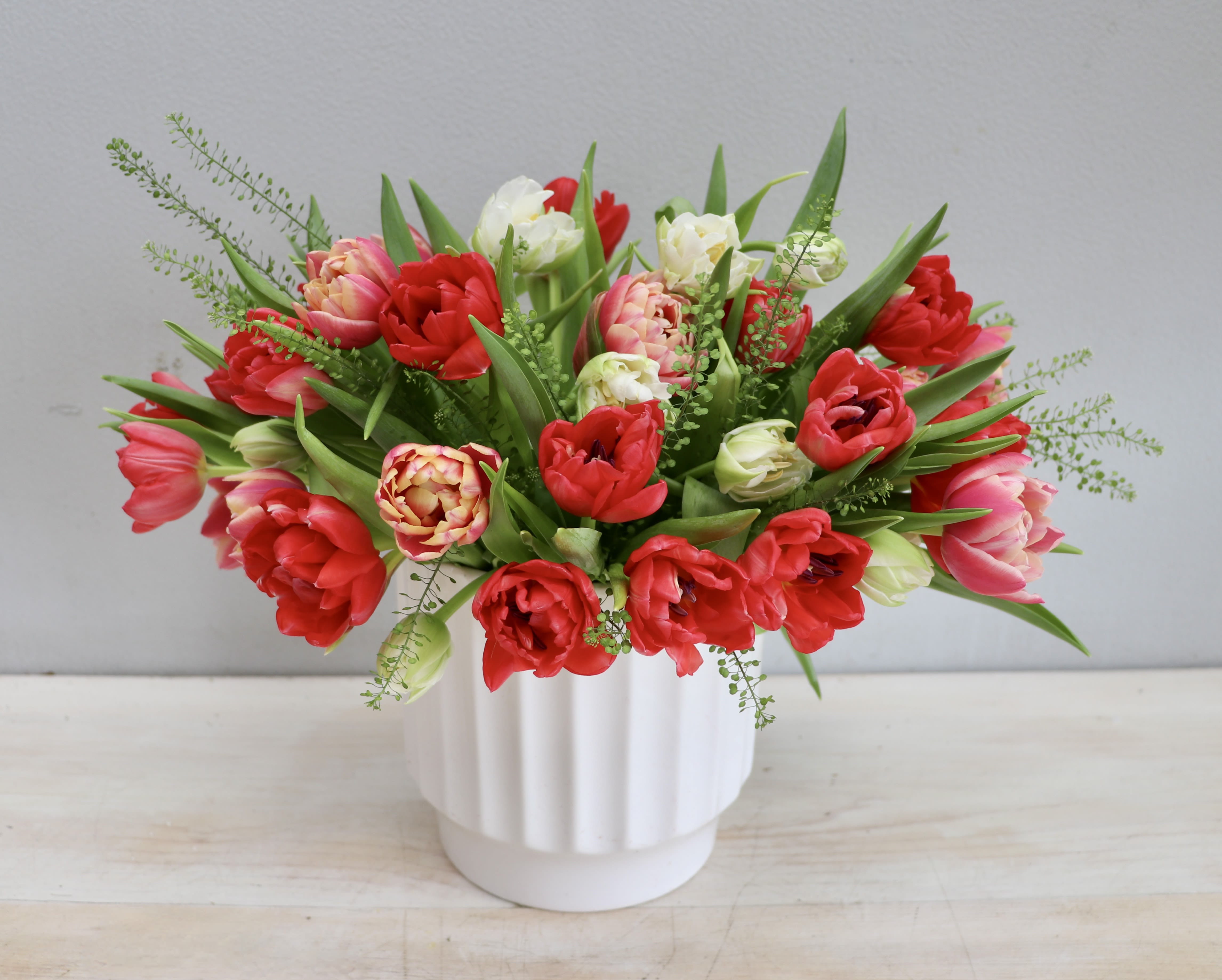 Wild at Heart - WeHo - This new design highlights beautiful red, pink, and white tulips in a classy ceramic vase. These bright tulips are artfully arranged with seasonal greenery. The standard size is about 12" tall.