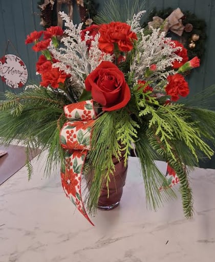 Under the Mistletoe - Make spirits bright with our Under the Mistletoe arrangement, designed in a striking tall red vase that captures the magic of the season. Lush holiday greens and long-lasting seasonal flowers rise gracefully, creating an elegant and romantic display. Accented with festive ribbons, and touches of winter charm, this arrangement brings the warmth of Christmas and a hint of holiday romance to any space. Perfect for gifting, decorating, or sharing a special moment under the mistletoe.