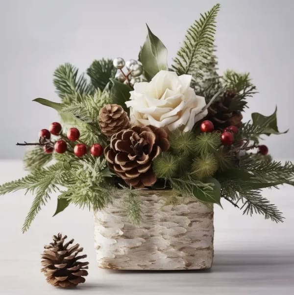 Simple Holiday Centerpiece - Minimal yet festive, our Simple Holiday Centerpiece features a stunning large white rose as the focal point, complemented by fresh seasonal greenery, bright red berry accents, and a natural pinecone. Designed in a square oak-toned base, this piece brings understated holiday charm and warmth to any table or space. Perfect for those who love clean, elegant seasonal décor with a cozy touch.