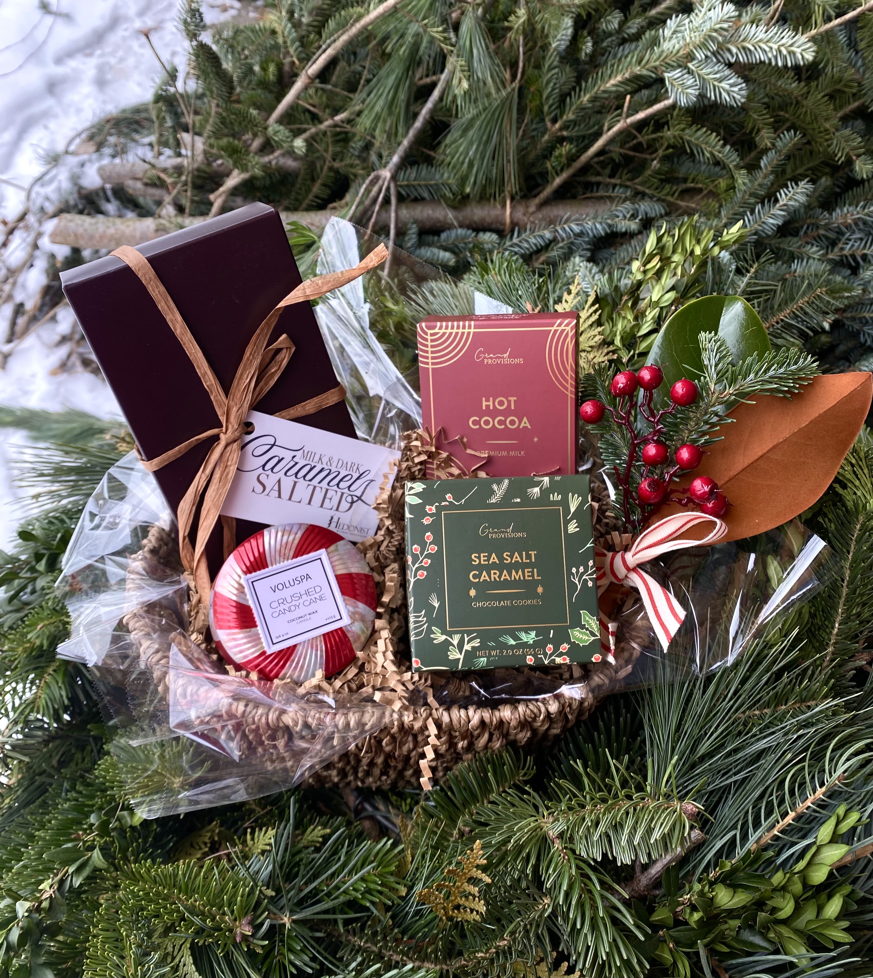 Sweet Treats - Perfect for the chocolate lover in your life! This gift basket contains one 4 oz Voluspa mini tin candle in Crushed Candy Cane, Sea Salt and Caramel Cookies, Two single serve sachets of Hot Cocoa, Hedonist Dark and Milk Chocolate Salted Caramels, and a Festive decorative berry sprig.