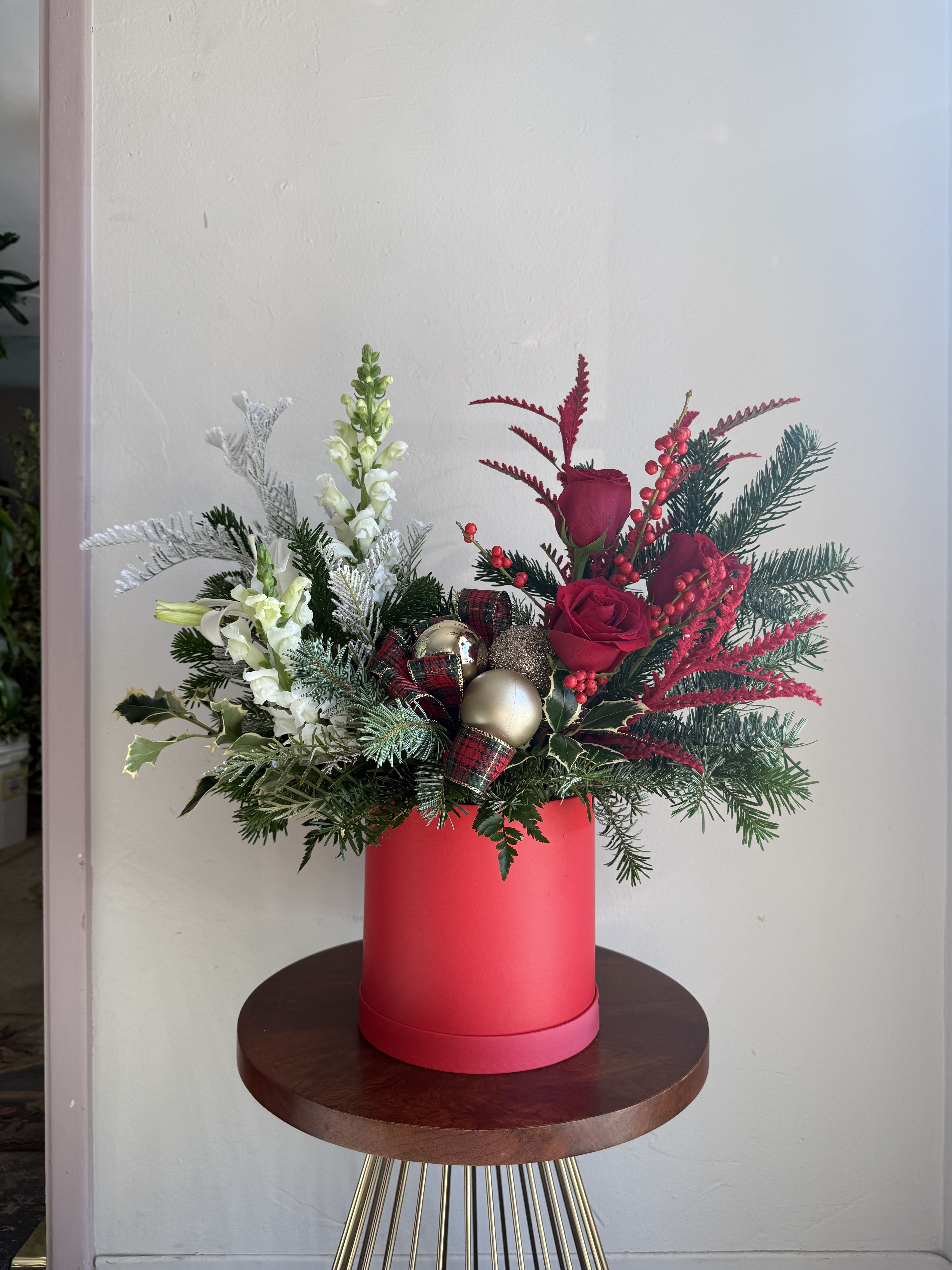Christmas Box - Christmas greens, frosted leaves, roses, lilies and snapdragons. Comes in a red or white box with ribbons and ornaments.   **Specific color can be requested** Please call or email to confirm.