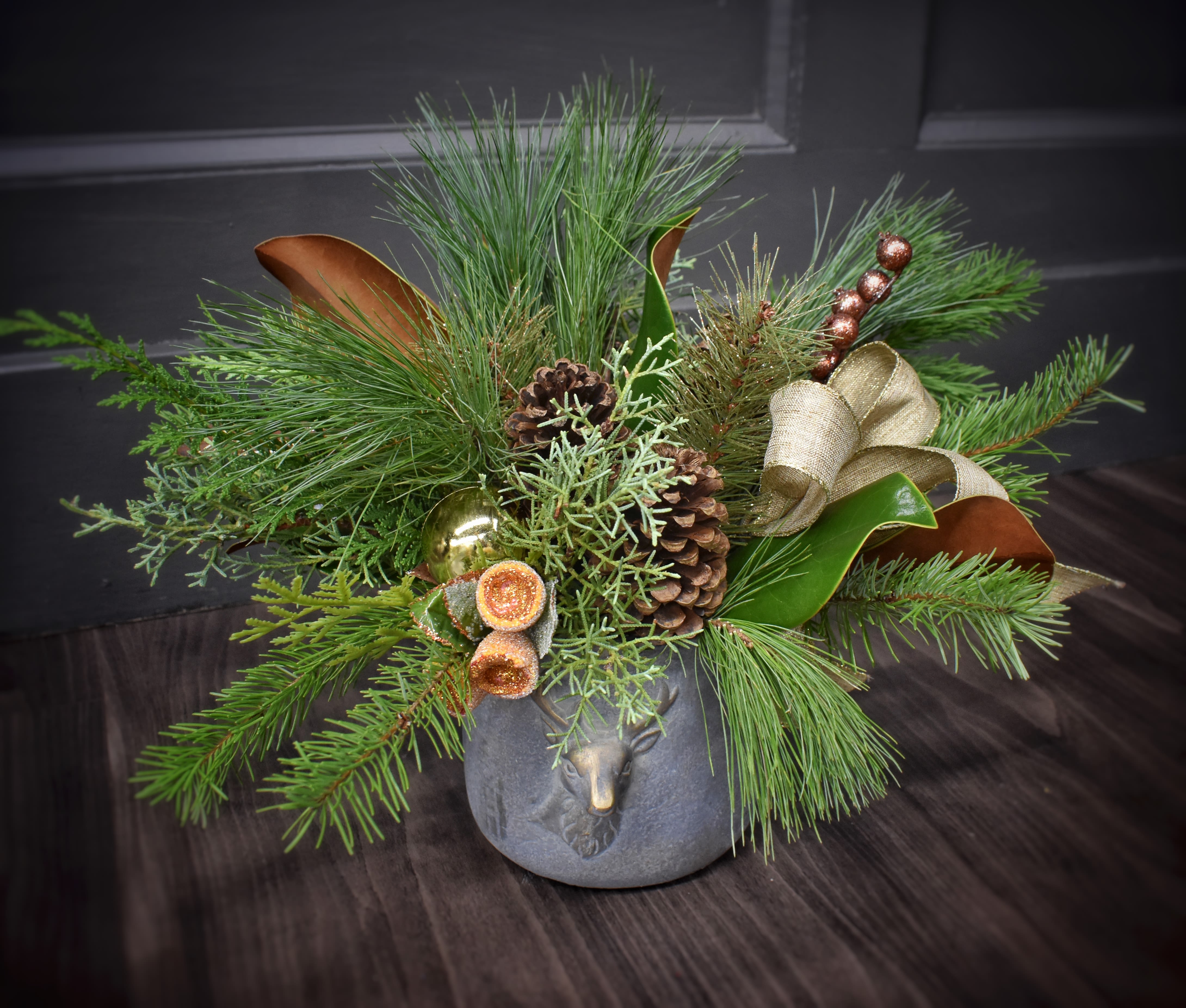 The Woodland Stag Bouquet - Just as a deer stands out boldly from the snow, this arrangement stands out from our others. An elegant mix of winter greenery, pinecones, and gold accents to compliment a gold brushed keepsake container. Upgrade to our deluxe edition to add 5 fluffy carnations. Our premium style features 3 luxurious red roses. 