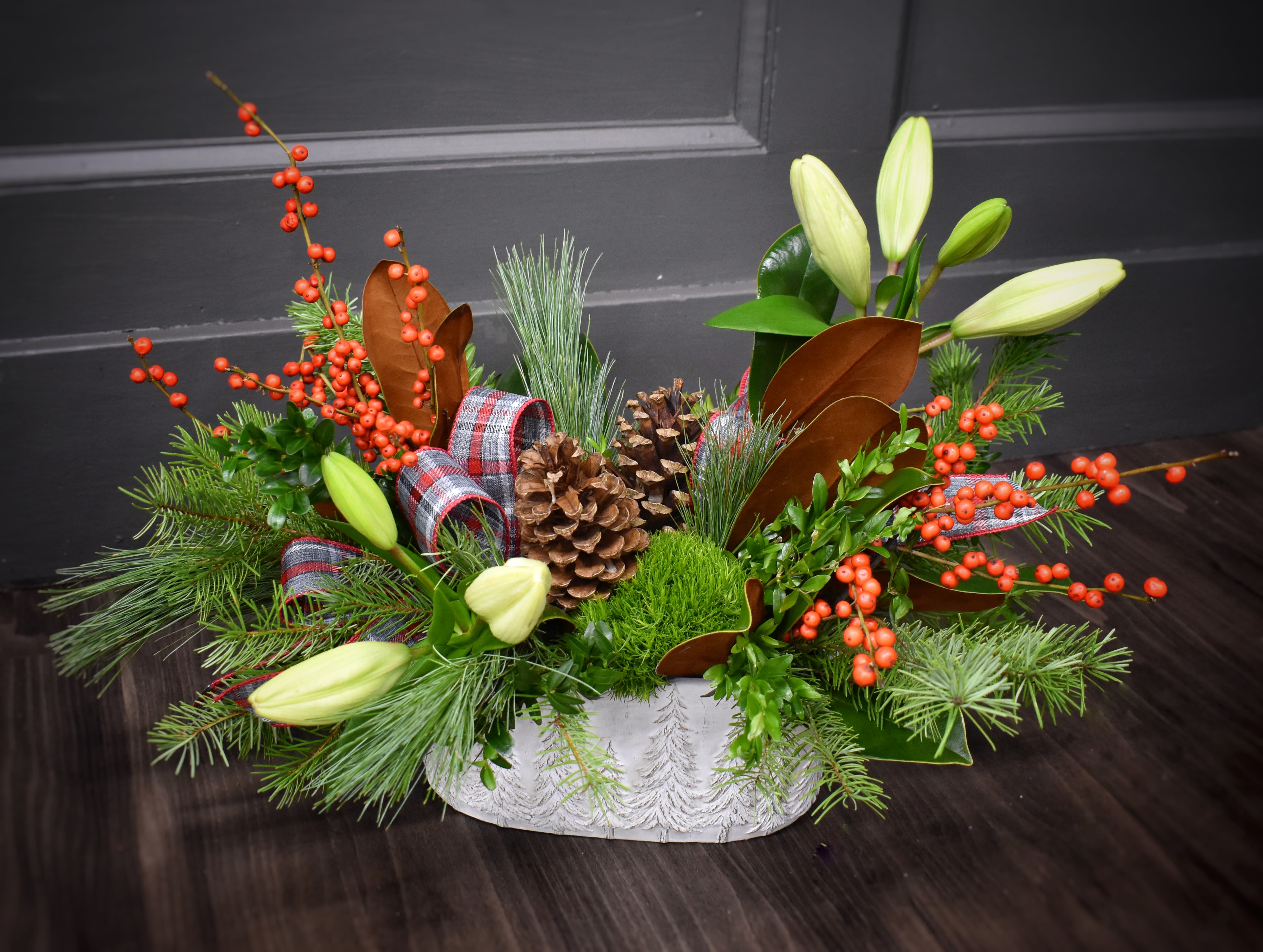 Deluxe Through the Woods  - &quot;Over the river and through the woods.&quot; Wherever you're going, this arrangement should come along. An excellent centerpiece for your holiday celebrations or just a merry display, this arrangement and its keepsake container will be the perfect fit for your home. This arrangement features a fragrant mix of evergreens, pinecones, ribbon, two large lilies, and fresh berries. 