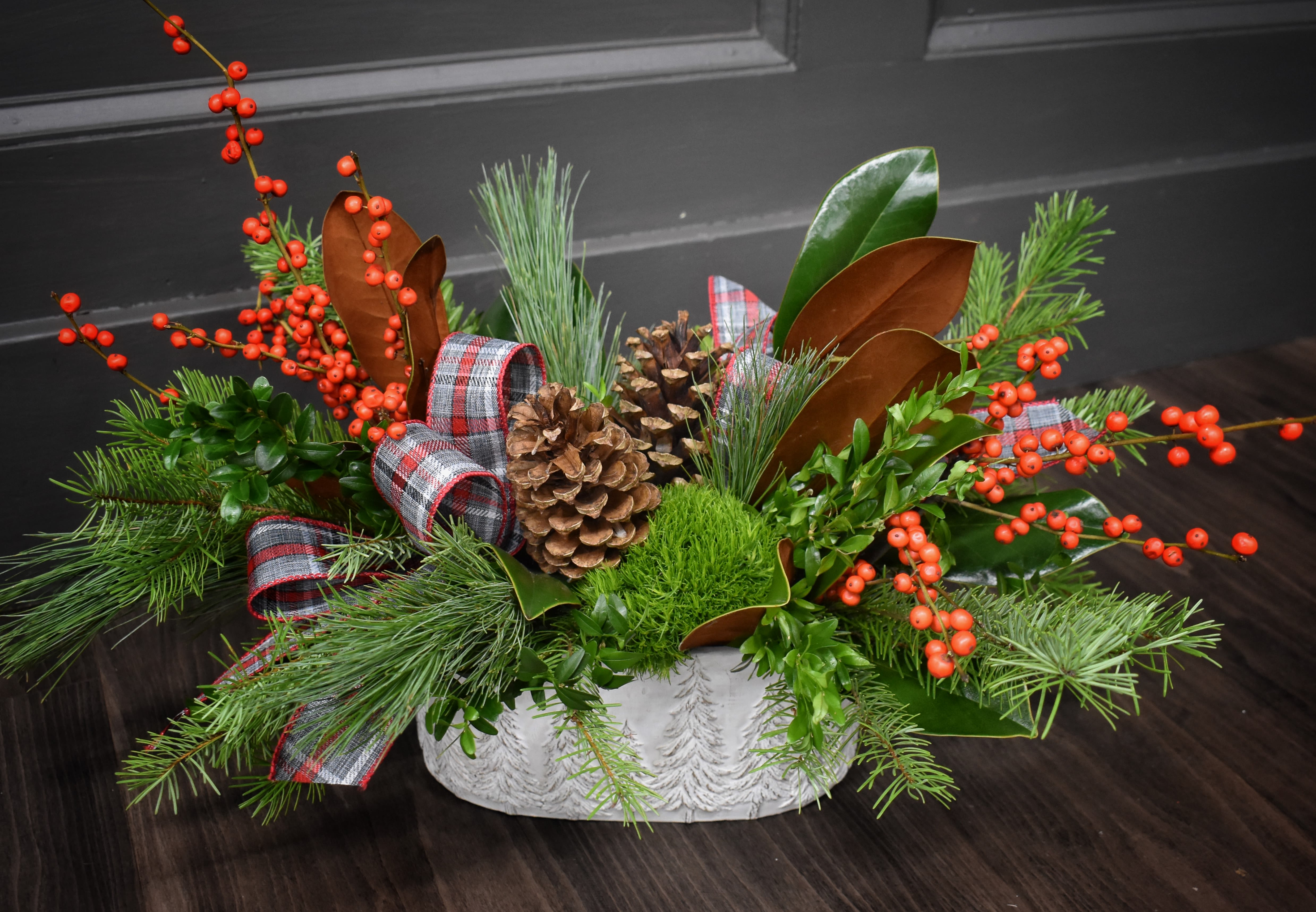 Through the Woods  - &quot;Over the river and through the woods.&quot; Wherever you're going, this arrangement wants to come along. An excellent centerpiece for your holiday celebrations or just a merry display, this arrangement and its keepsake container will be the perfect fit for your home. This arrangement features a fragrant mix of evergreens, pinecones, ribbon and fresh berries. Upgrade to our deluxe edition and we'll add two large white lilies. Our premium version features 4 additional luxurious red roses. 
