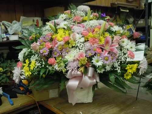 TB30 Sympathy Basket - A mixture of white, lavender and yellow daisies, pink carnations, pink roses, white fuji mums, yellow alstromaria, baby's breath, greens and lavender bow  Banner - $15.00 + extra  Substitutions may apply due to flower availability