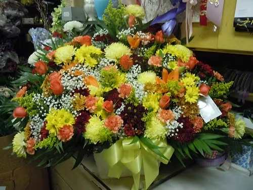 TB32 Sympathy Basket - A mixture of yellow, bronze and burgandy daisies, orange carnations, orange roses, yellow fuji mums, baby's breath, yellow solidago, greens and yellow bow   Banner - $15.00 + extra   Substitutions may apply due to flower availability