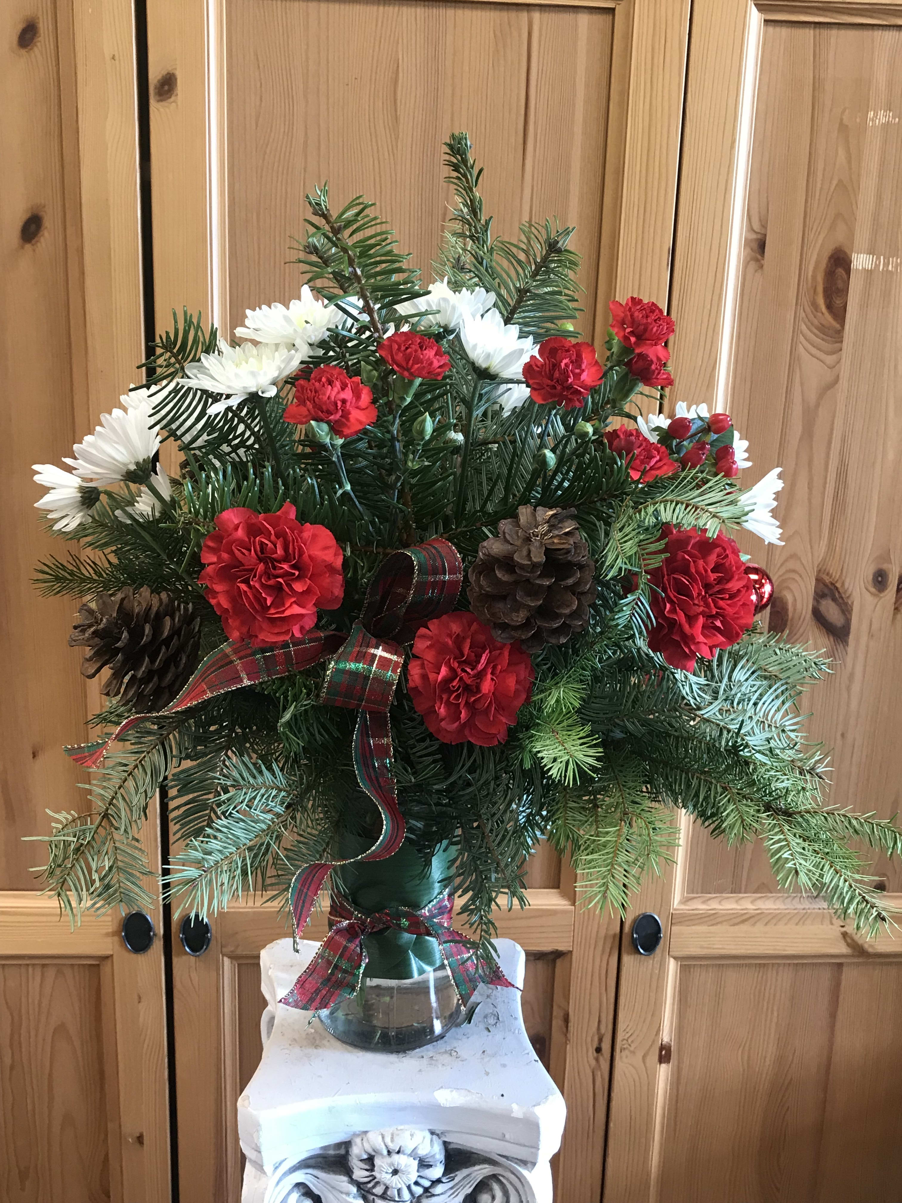 Holiday Happiness - When thinking of a great gift, send our Holiday Happiness vased arrangement. Just the right touch for family or business gift giving. The vased  arrangement. Includes all the trimmings. Winter greens, ornaments, pine cones, hypericum, carnations, mums, and sparkly ribbon. 