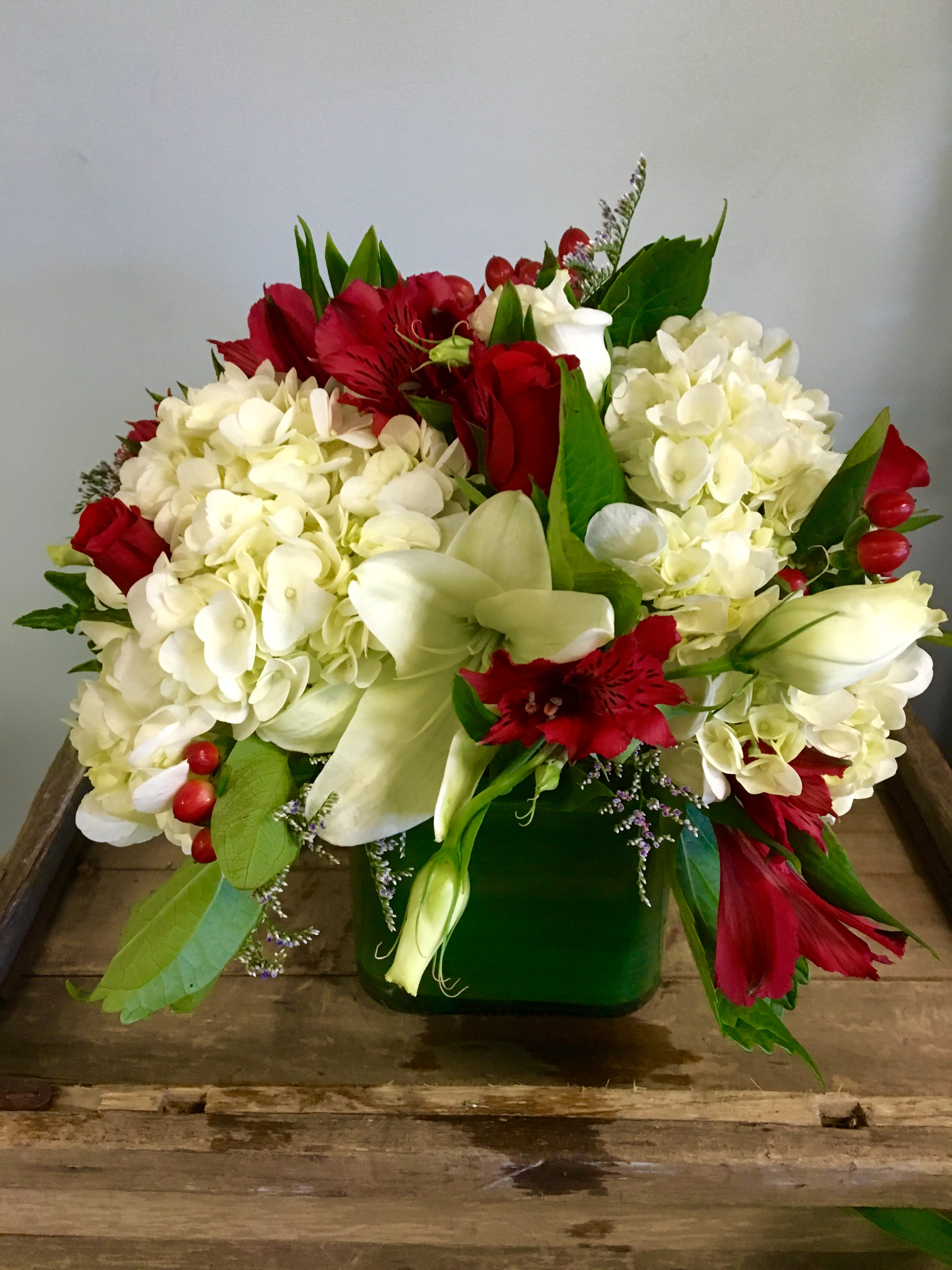 'Tis The Season - Spread the holiday cheer with this beautiful centerpiece. Designed low and compact, bursting with hydrangeas, lilies, roses, and seasonal decorative accents. Arrives in a glass cube wrapped with a leaf. Can't go wrong! 