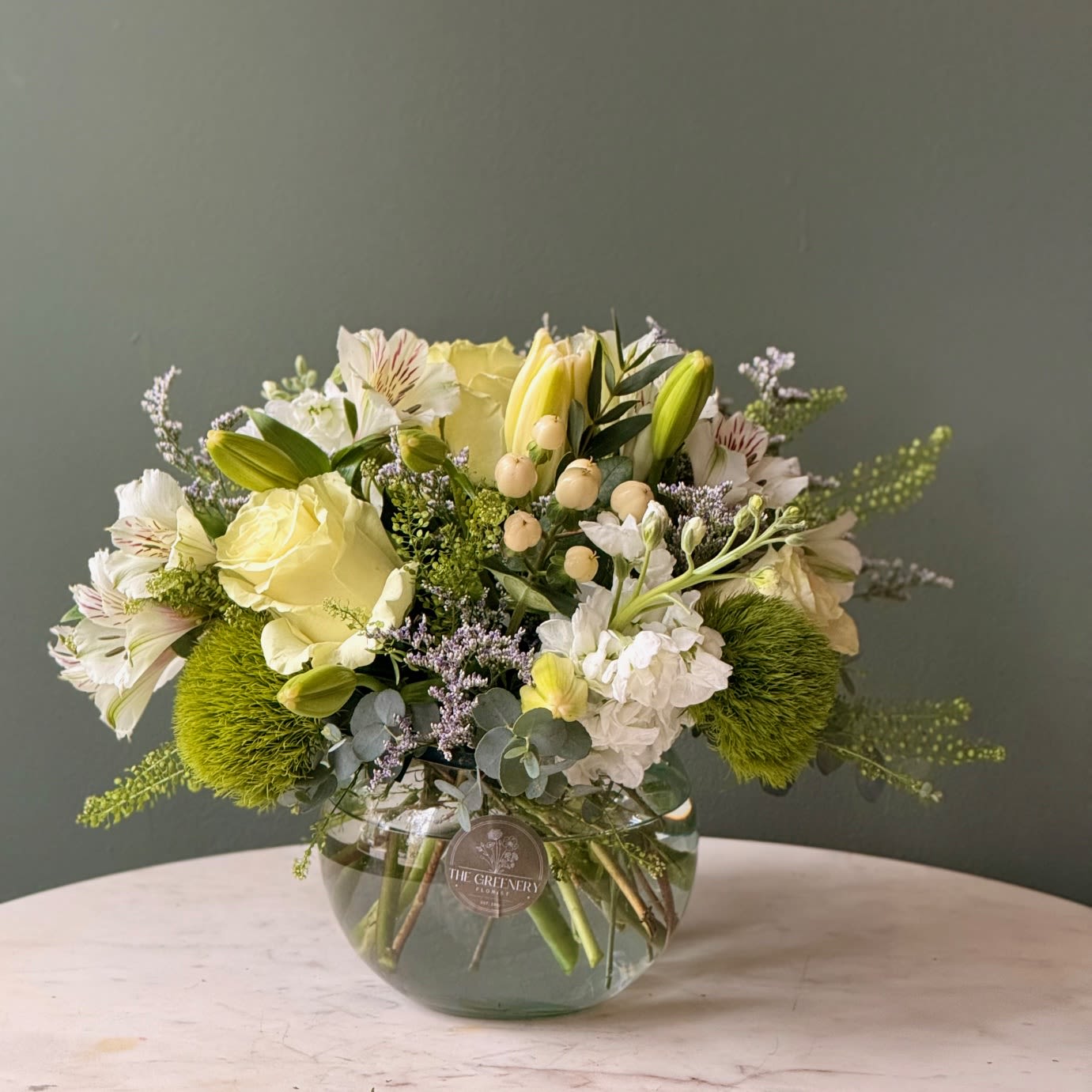 Folly Breeze -  A soft, all in white and green floral design for moments that deserve a touch of elegance. Featuring: - Ecuadorian Roses - Hypericum - Green Trick - Stock - Alstroemeria - Styled with premium seasonal foliage Presentation Options: Short clear bowl measures approximately 5&quot; H. Vase included in price. Every order includes: A custom message card - simply enter your message at checkout and we'll take care of the rest. Please note: Flowers are subject to seasonal availability. If a listed flower is unavailable, our designers will substitute it with flowers of a similar shape, color, and style to maintain the overall aesthetic.