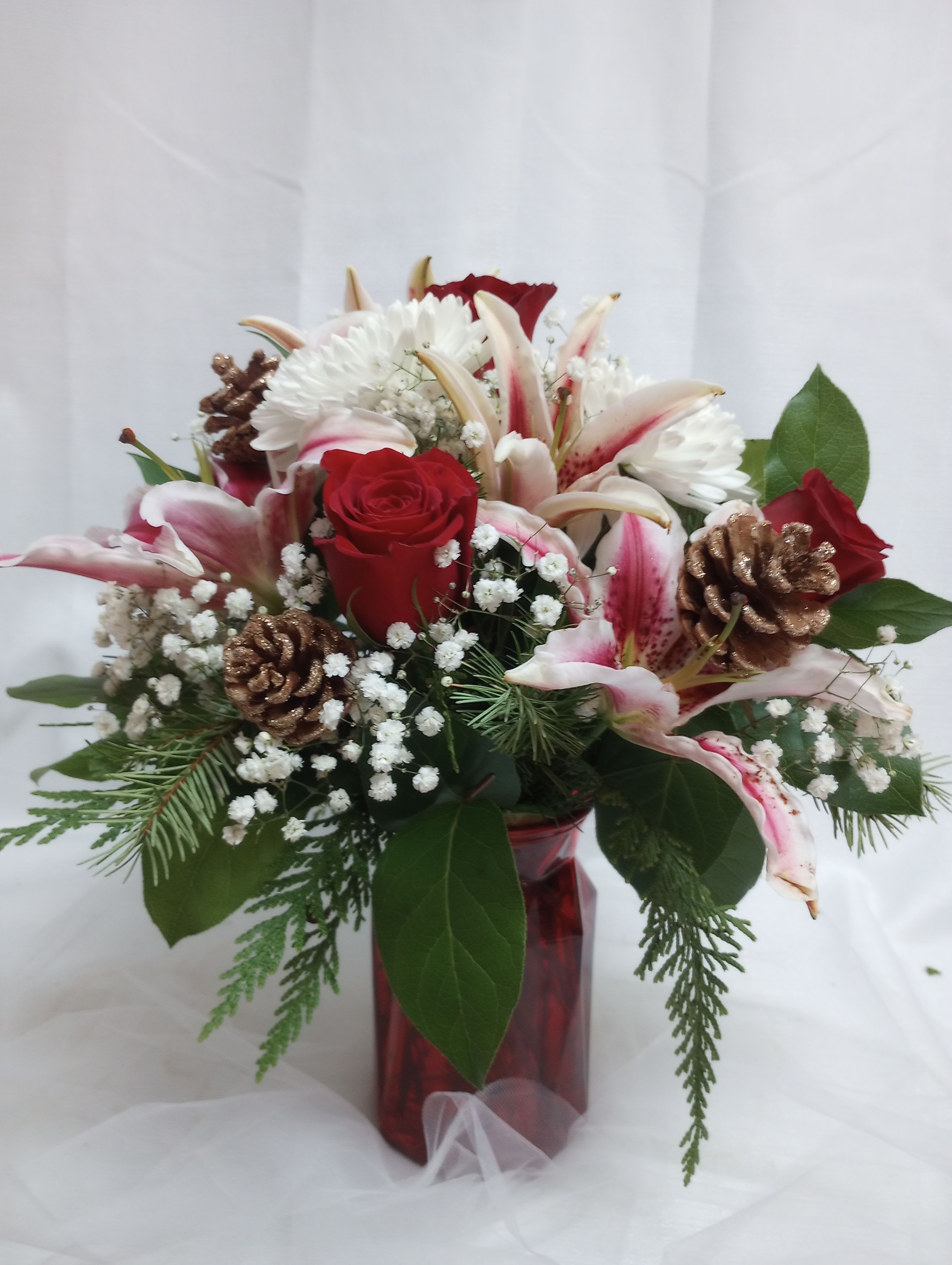 Velvet Noel - Celebrate the season with this vibrant display of red roses and hot pink lilies! This cheerful arrangement, accented with assorted evergreen branches and a touch of festive flair, is the perfect way to spread holiday joy and cheer.