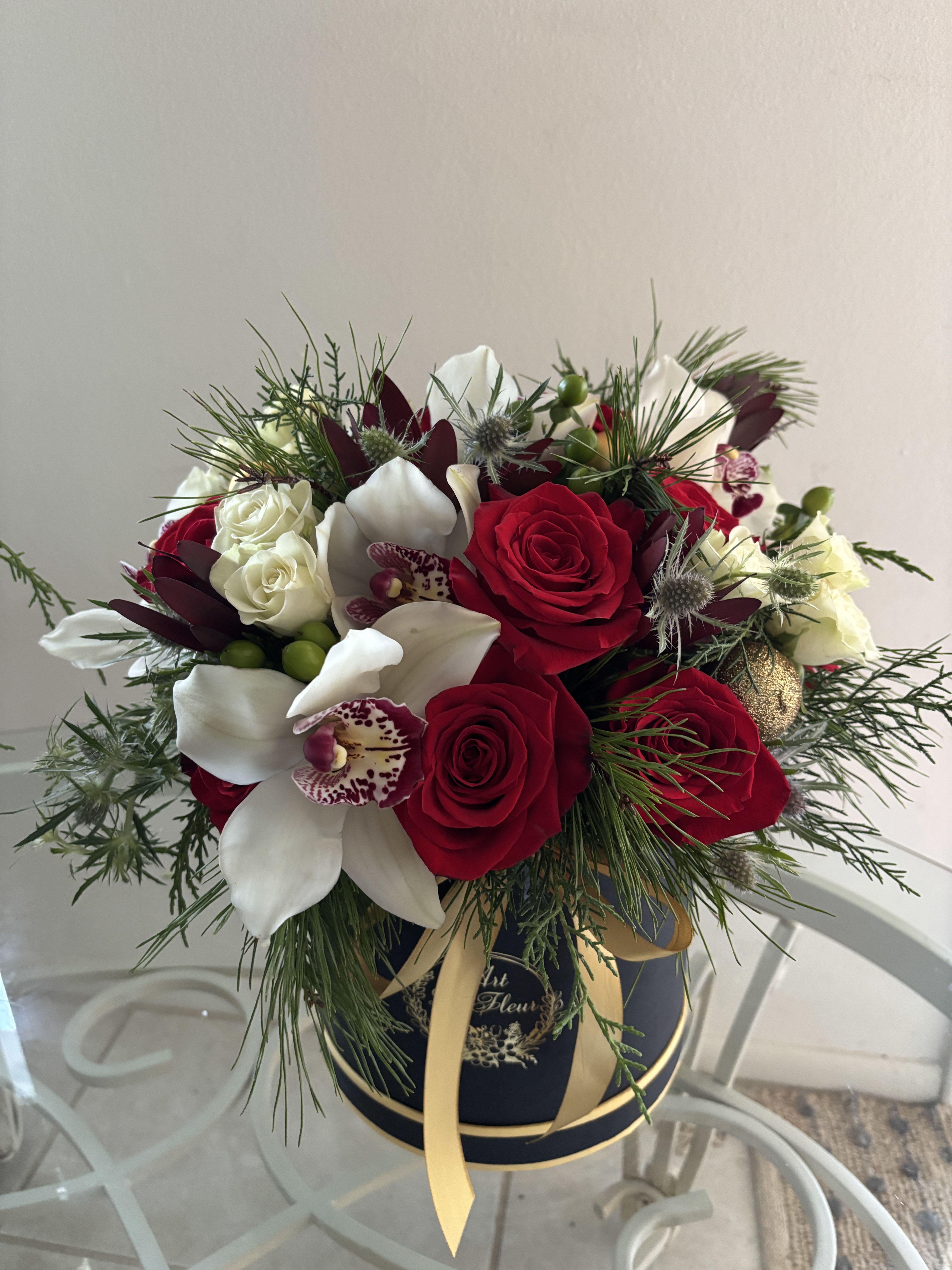 Holidays Classic Elegance - Presented in an elegant black and gold hatbox, this arrangement blends premium holiday greens with striking red and white flowers for a refined, modern twist on traditional Christmas florals.Perfect for gifting or elevating your holiday décor.