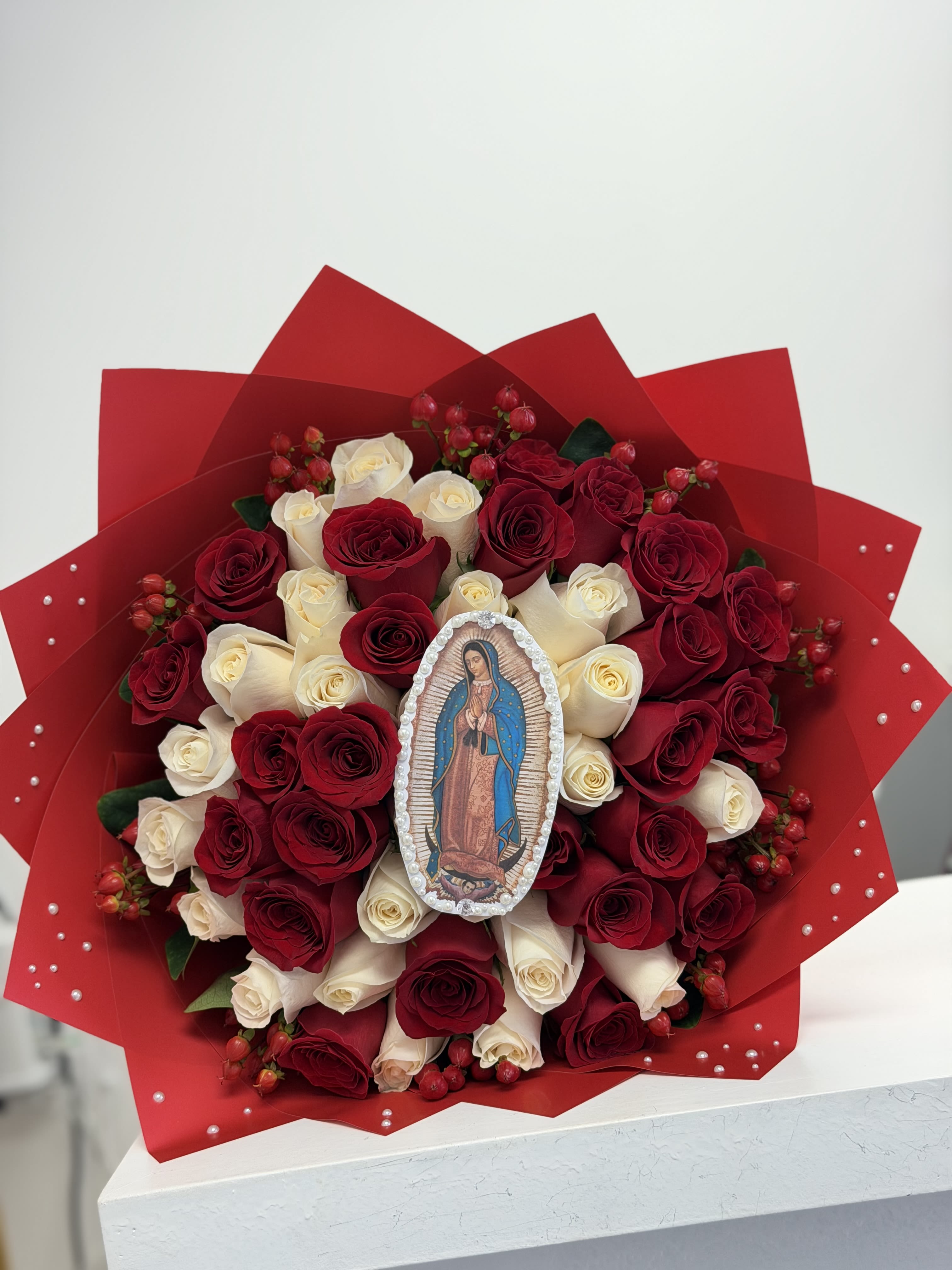 Virgen de Guadalupe Bouquet  - Un arreglo lleno de fe, belleza y simbolismo. Nuestro Bouquet Virgen de Guadalupe está cuidadosamente elaborado con 25 rosas rojas y 25 rosas blancas, creando un contraste armonioso que representa amor, pureza y devoción. En el centro del bouquet destaca una imagen de la Virgen de Guadalupe, convirtiéndolo en un arreglo perfecto para ofrendas, celebraciones religiosas y momentos especiales en su honor. 