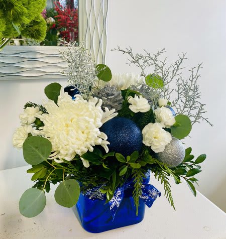 Blue  Christmas - This winter design features fresh green and white blooms, fragrant holiday greenery and frosted pinecones arranged in a beautiful blue glass vase.
